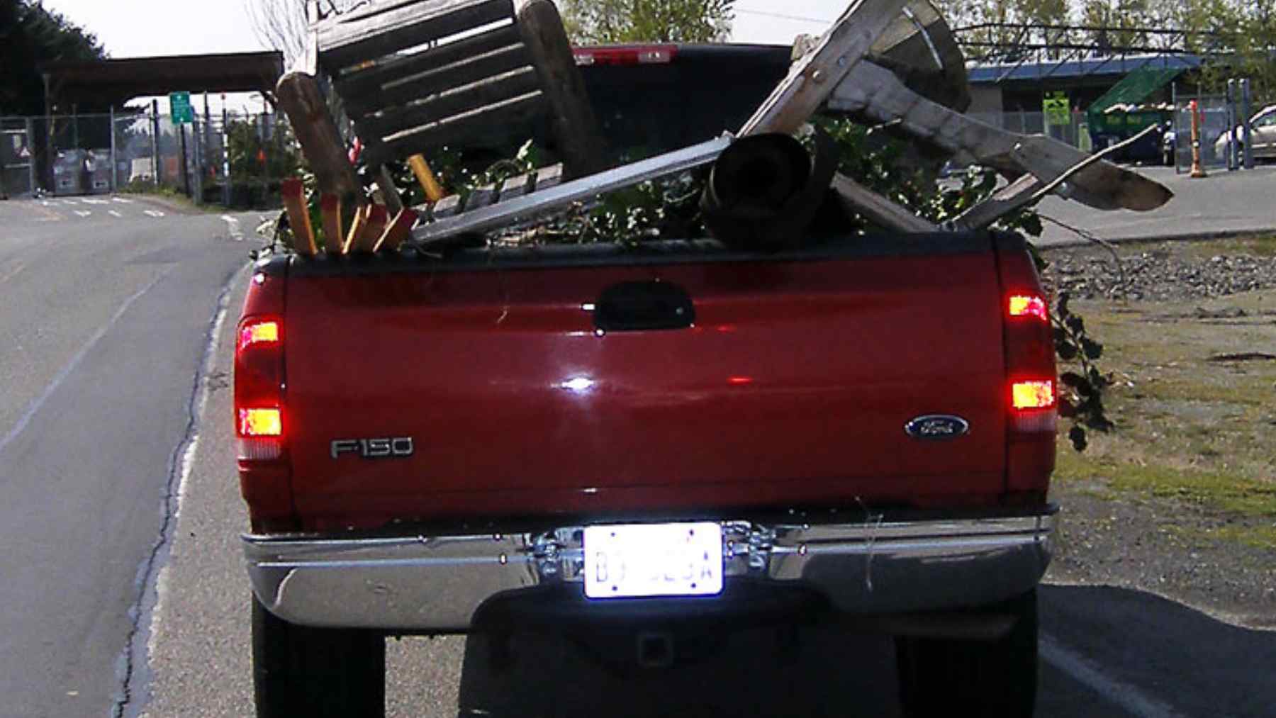 Overloaded red pickup truck with unsecured debris in the bed, illustrating the danger of loose cargo on highways.