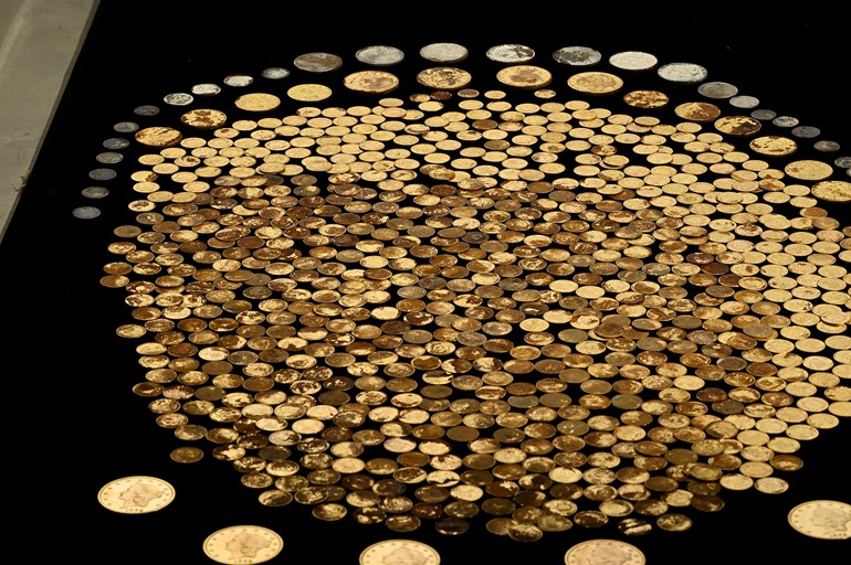 Hundreds of Civil War era coins, mostly gold, laid out in a large circle on a black surface as part of the Great Kentucky Hoard.