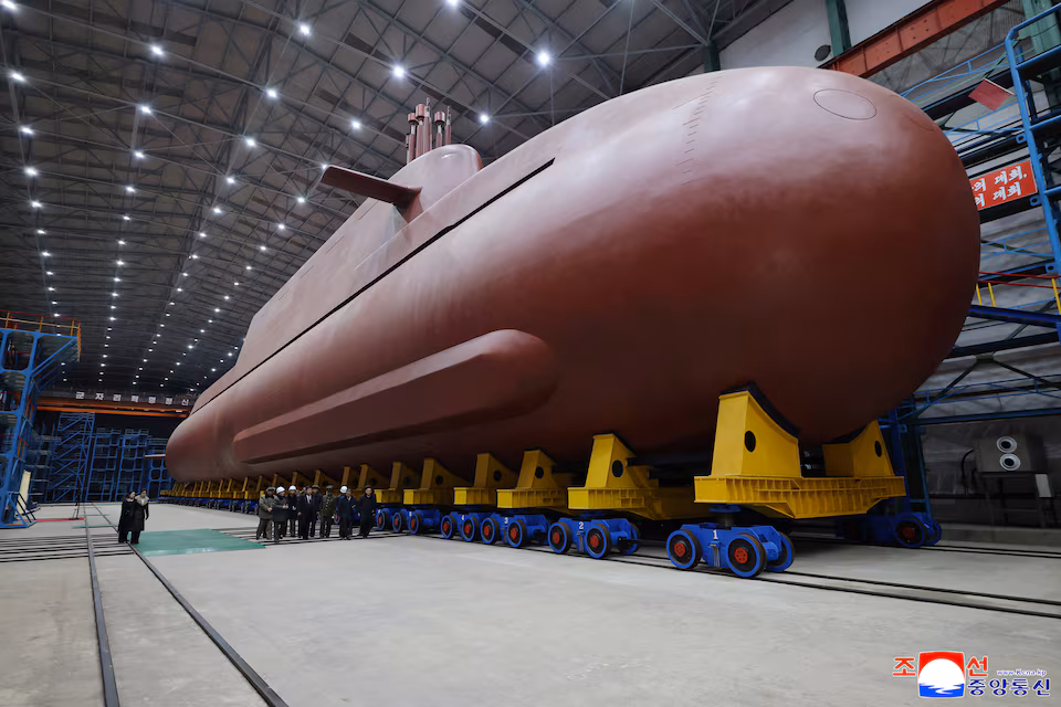 North Korean leader stands inside an indoor shipyard beside a large submarine hull shown in newly released state media photos.