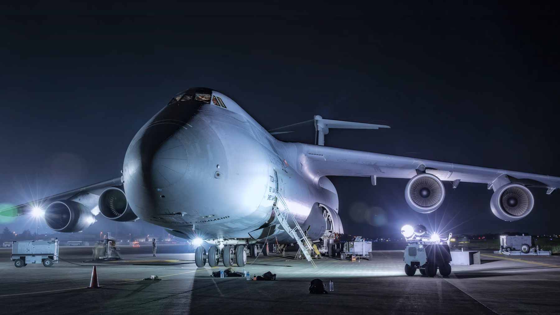 U.S. Air Force C-5M Super Galaxy cargo plane on the runway at night with ground crews and floodlights around the aircraft.