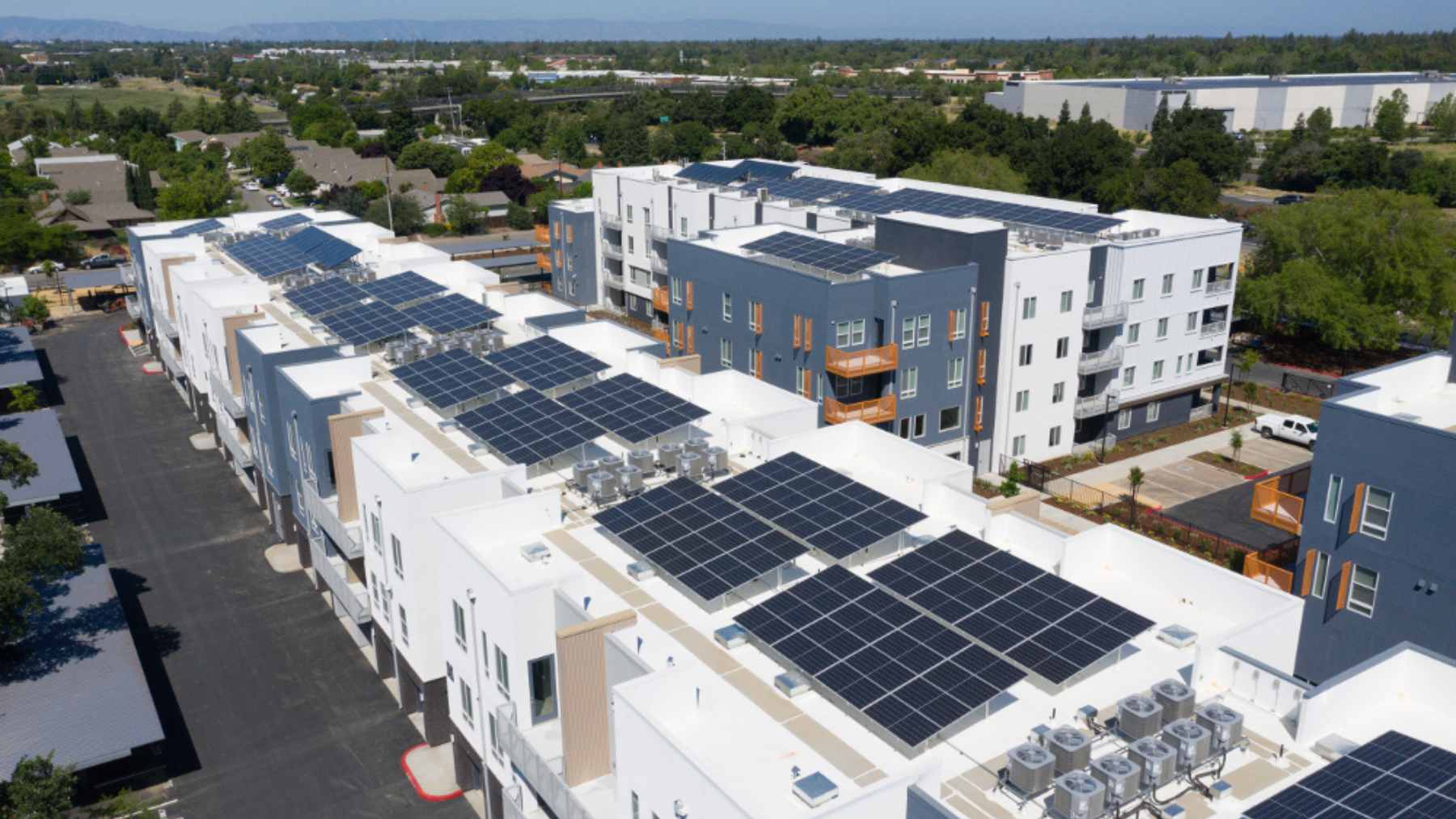 Aerial view of a California apartment complex with large rooftop solar arrays covering multiple flat buildings.