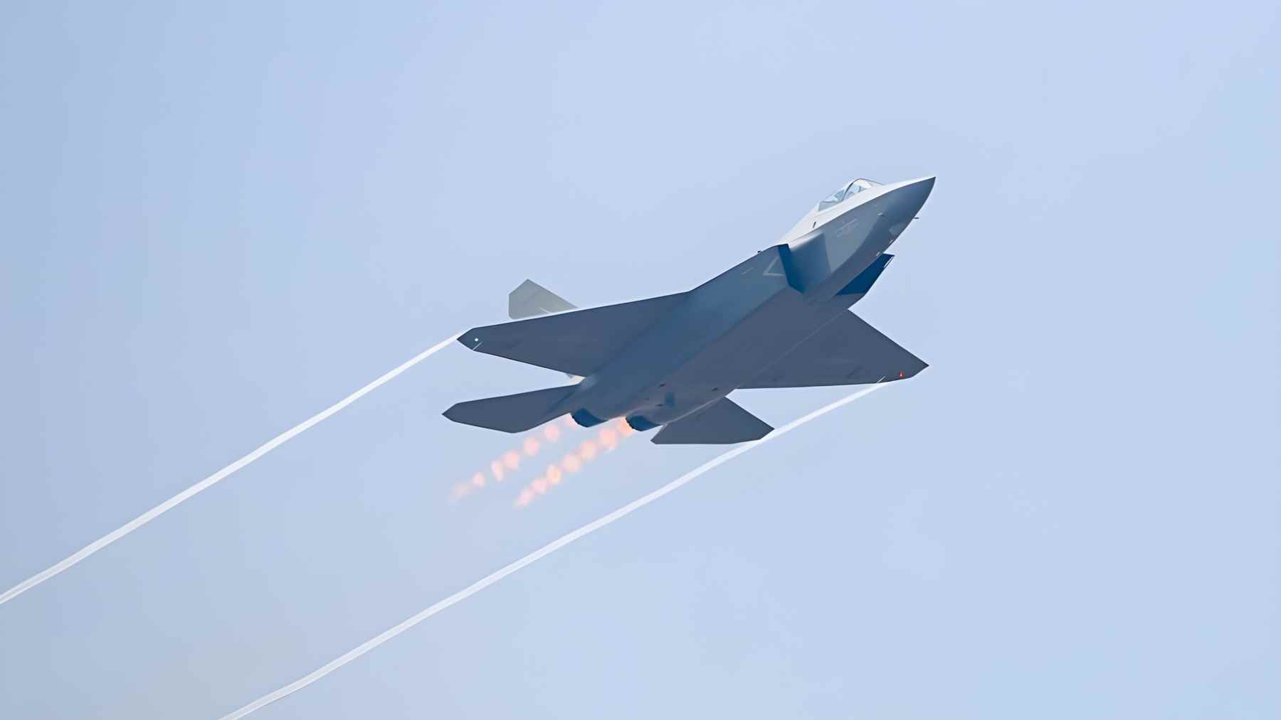 Chinese stealth fighter jet in flight with afterburner and contrails, illustrating the carbon footprint of modern military aviation
