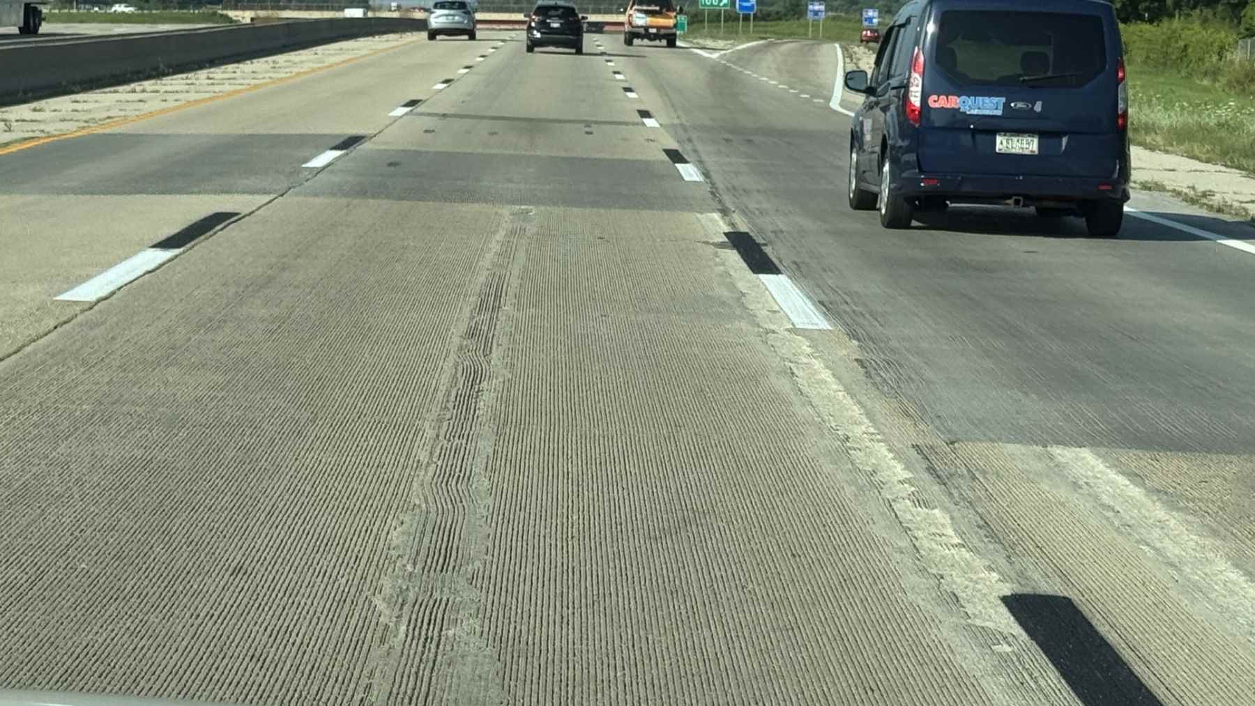 Concrete interstate lane with white dashed lines paired with thin black bands, a contrast marking that stays visible in glare.