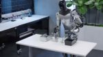 Tesla’s Optimus humanoid robot works at a lab table during a demo, showing AI-driven hands handling small parts.