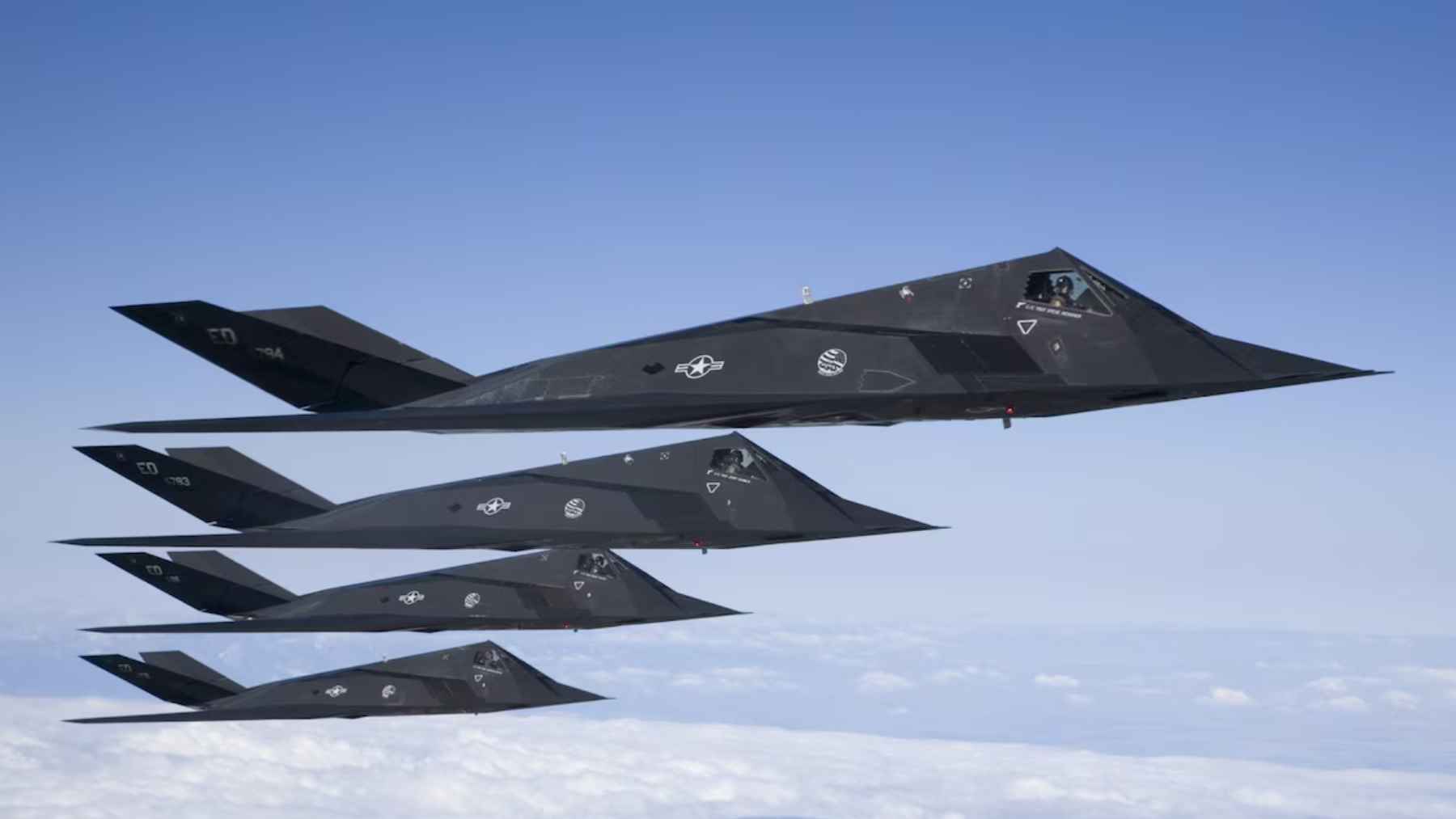 Four F-117 Nighthawk stealth jets fly in formation above clouds during a US Air Force training mission.