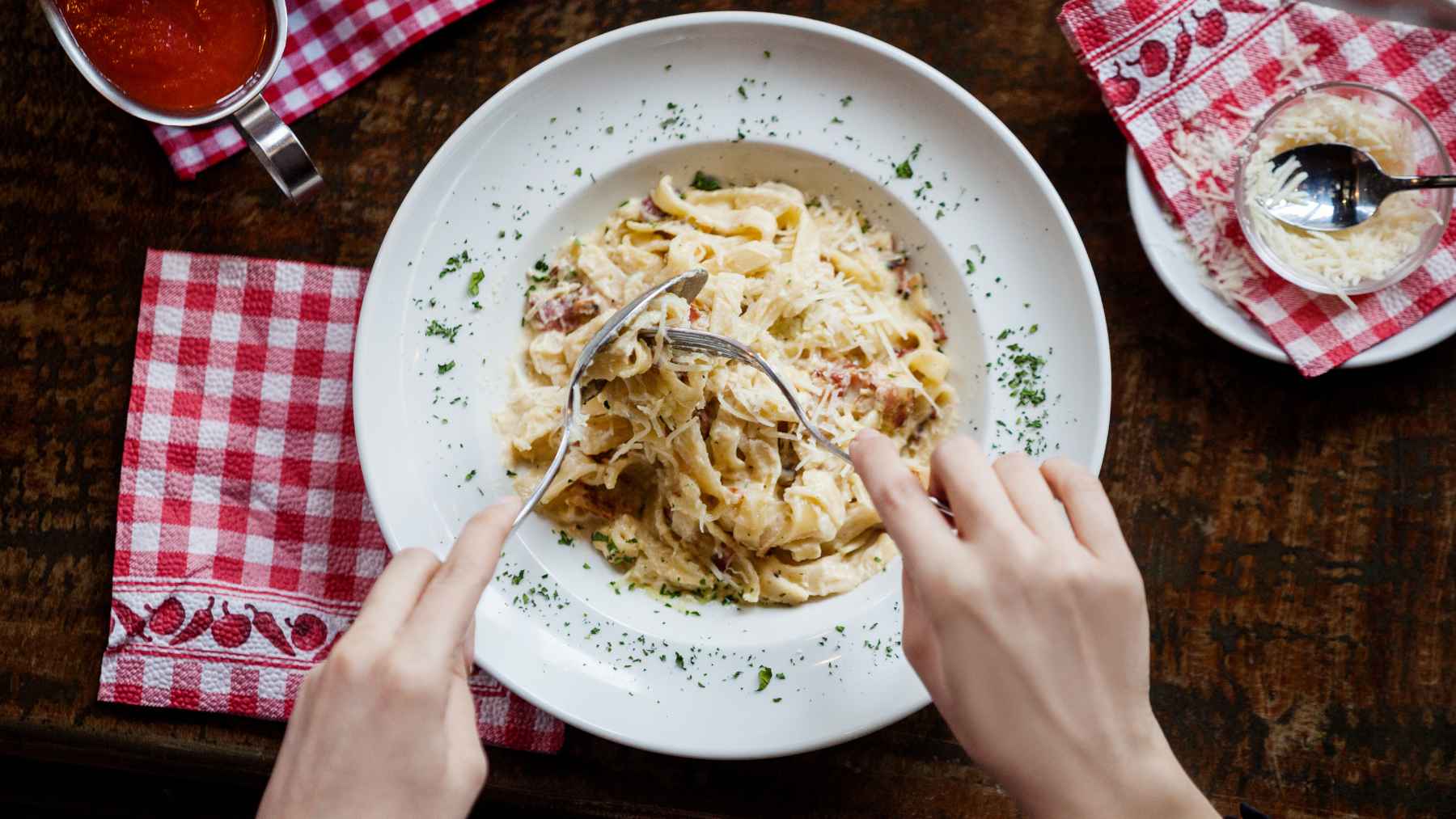 Hands twirling pasta topped with grated Pecorino Romano cheese, the type involved in an FDA listeria recall.