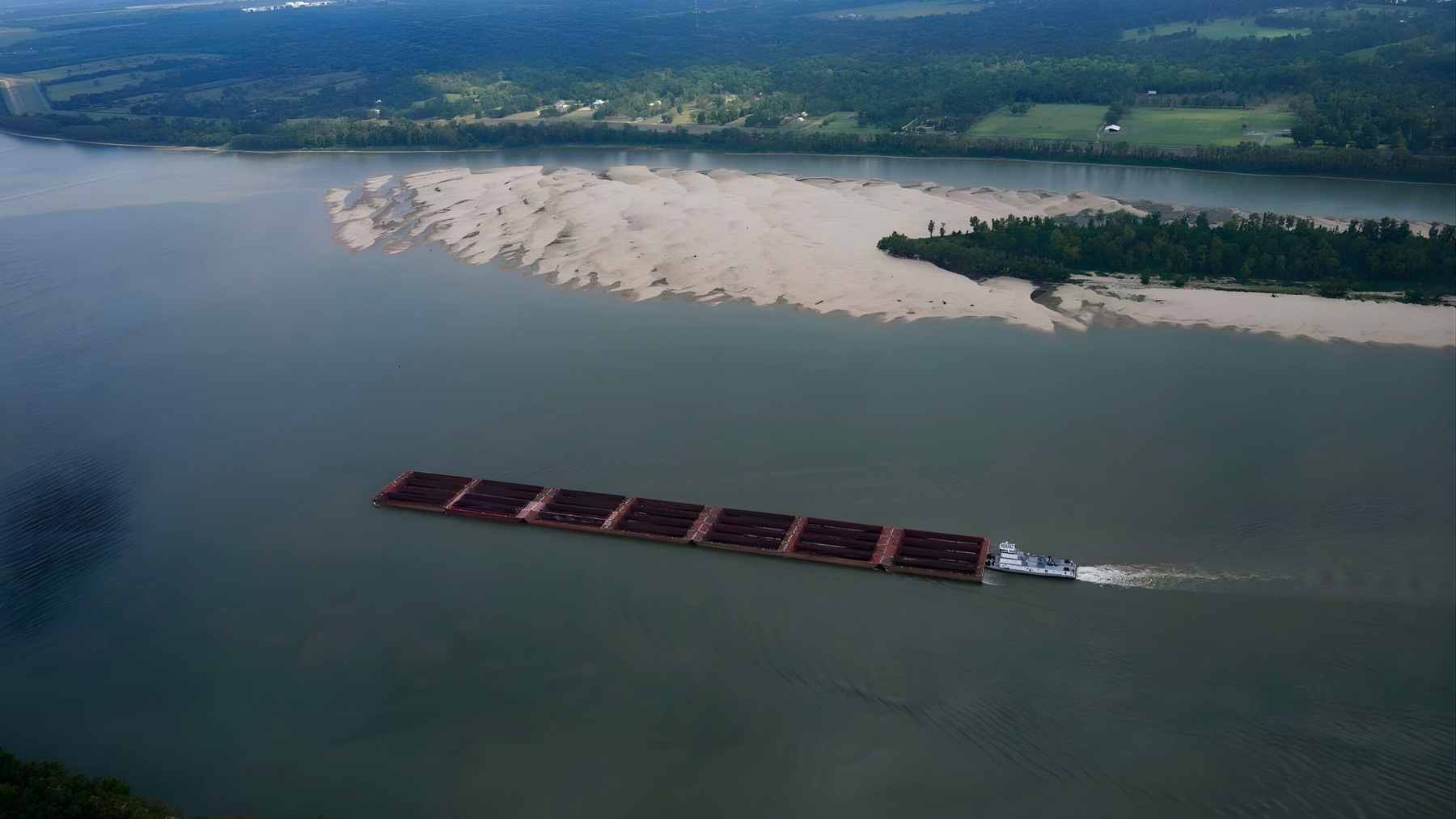 A barge moves along the Mississippi River near sandbars and a growing crevasse delta in coastal Louisiana.