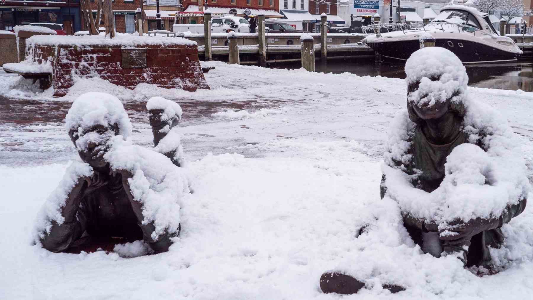 Snow-covered waterfront statues in Maryland as forecasters monitor a coastal system that could bring weekend snow