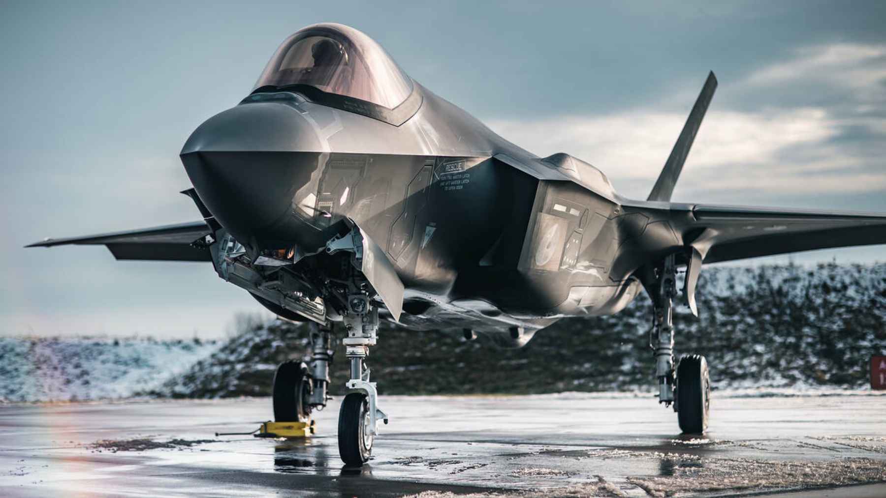 An F-35A stealth fighter sits on a wet runway in cold conditions, photographed during a military training deployment.
