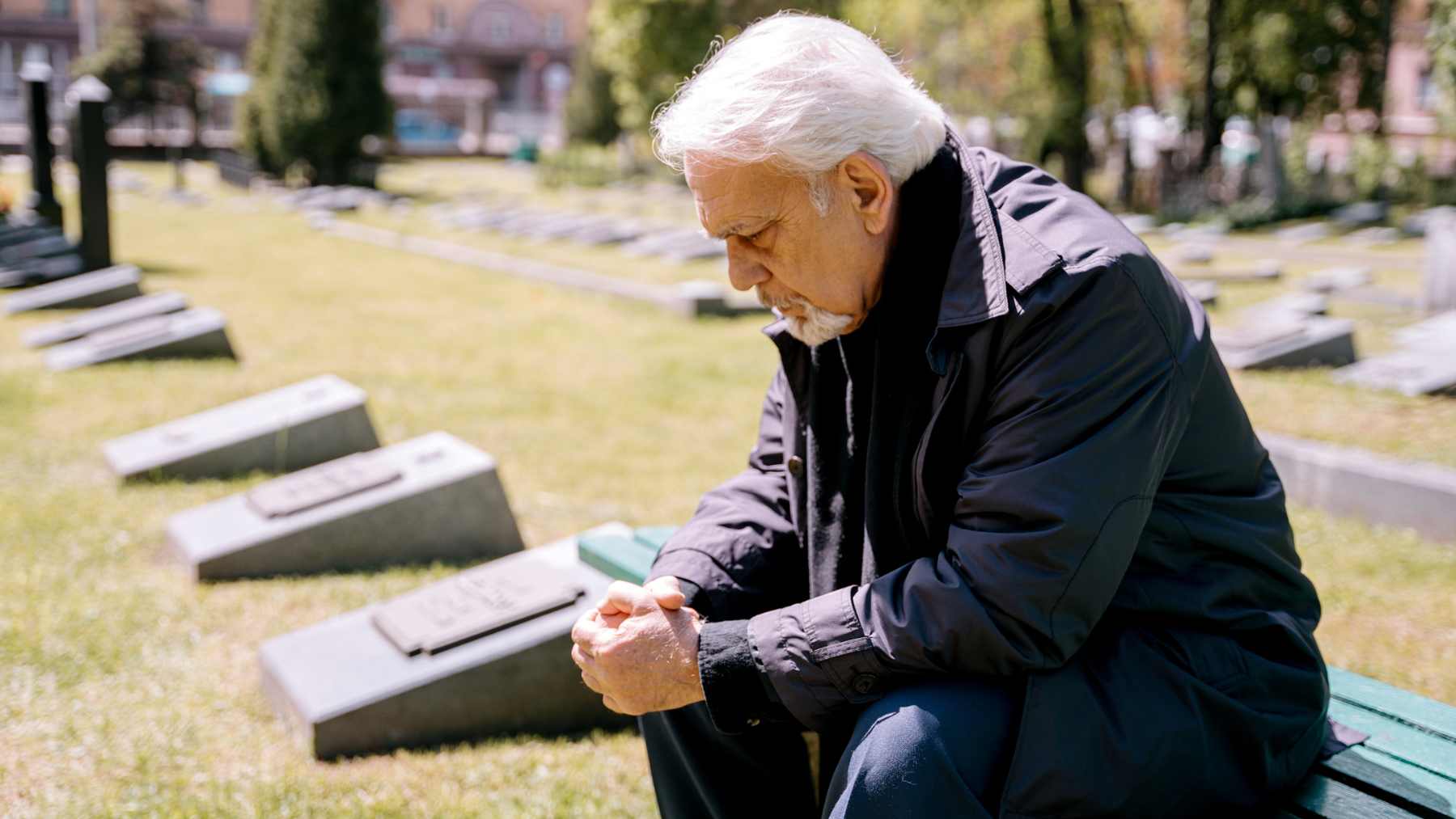 Older man sits alone on a bench in a cemetery, head bowed, reflecting on loss, identity, and the emotional shock that can follow retirement.