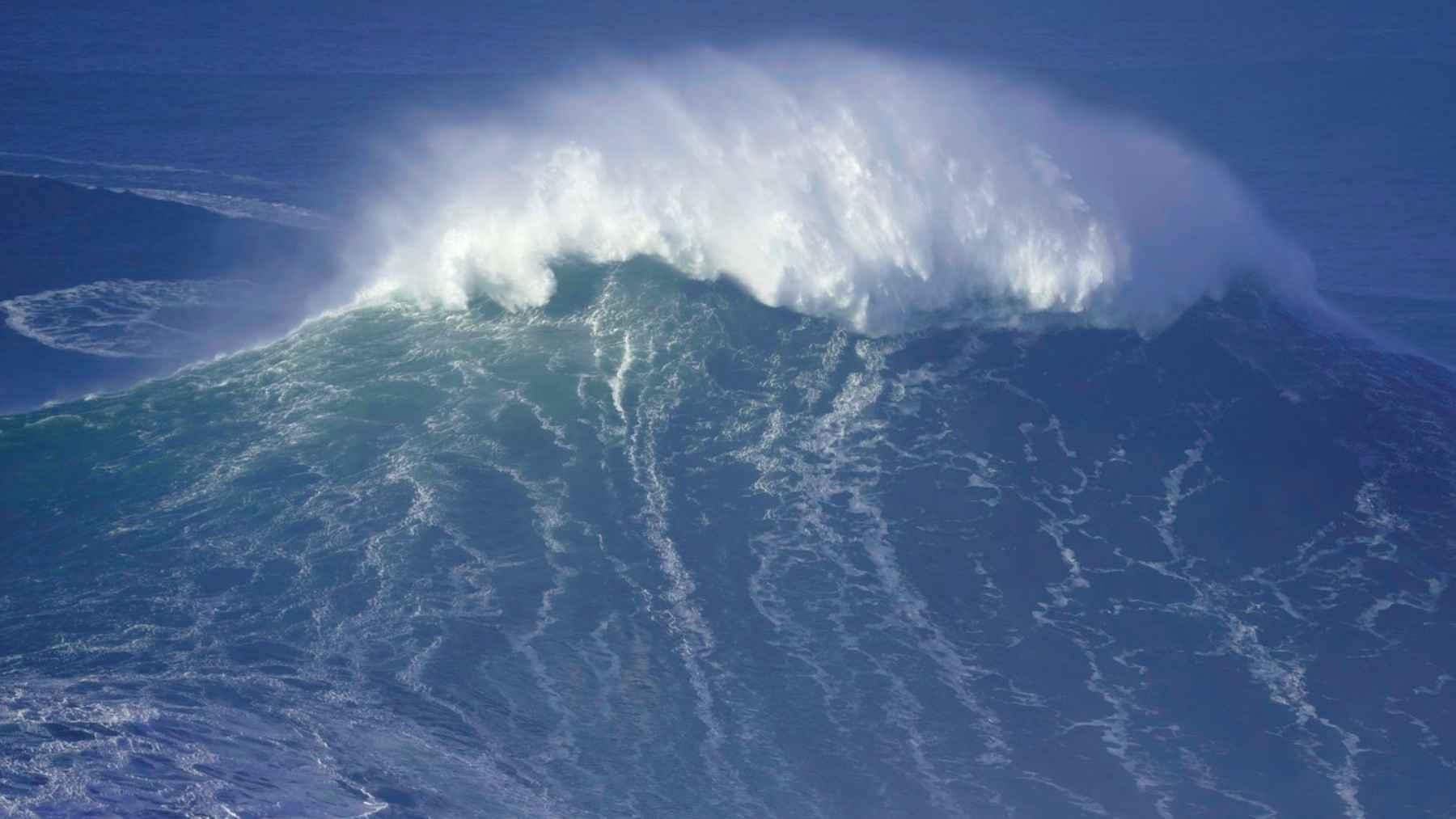 Towering open-ocean wave with windblown spray, part of the North Pacific megastorm swell measured at up to 115 feet.