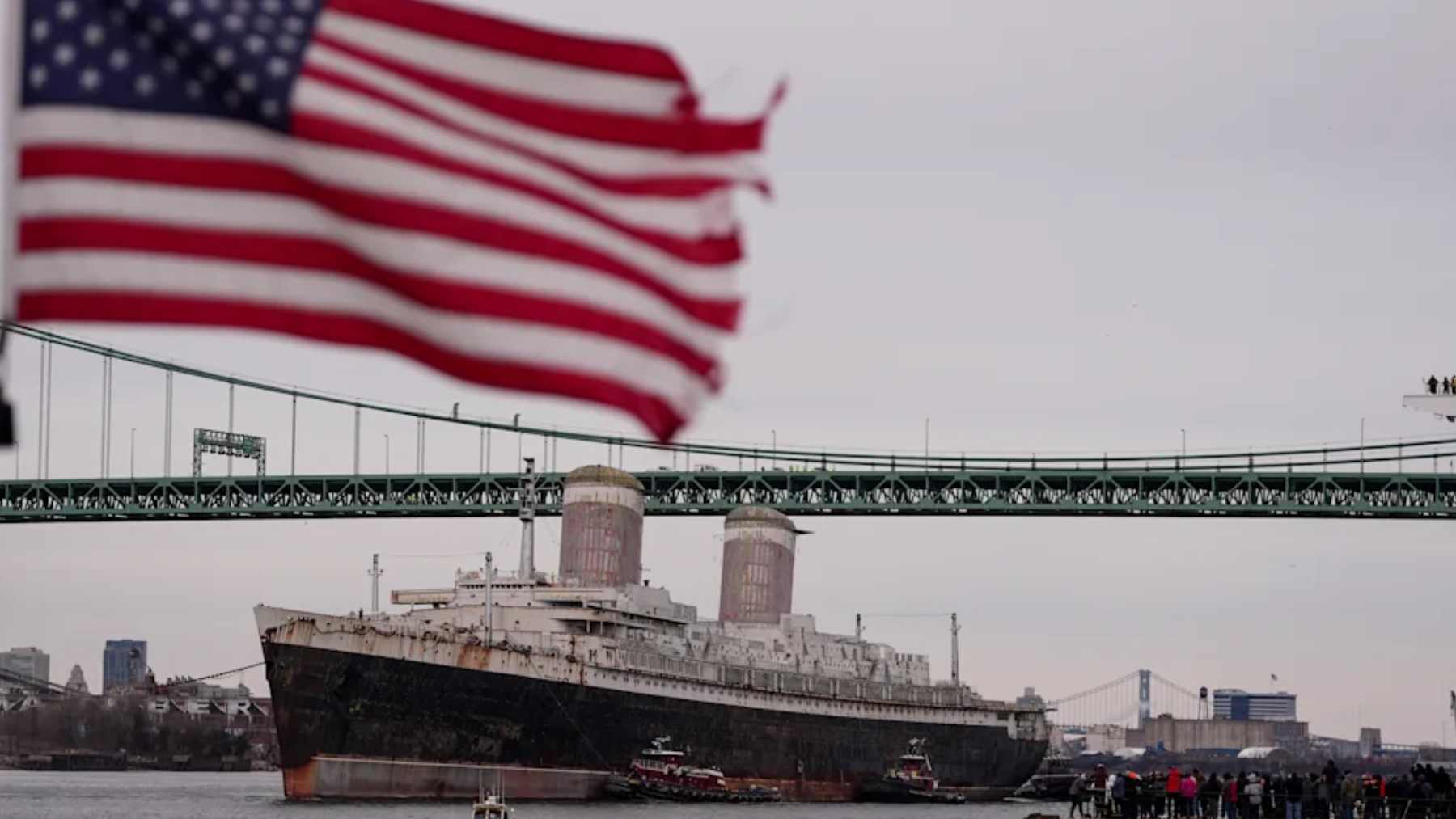 The ocean liner SS United States passes beneath a Delaware River bridge as it departs for conversion into a Gulf artificial reef.