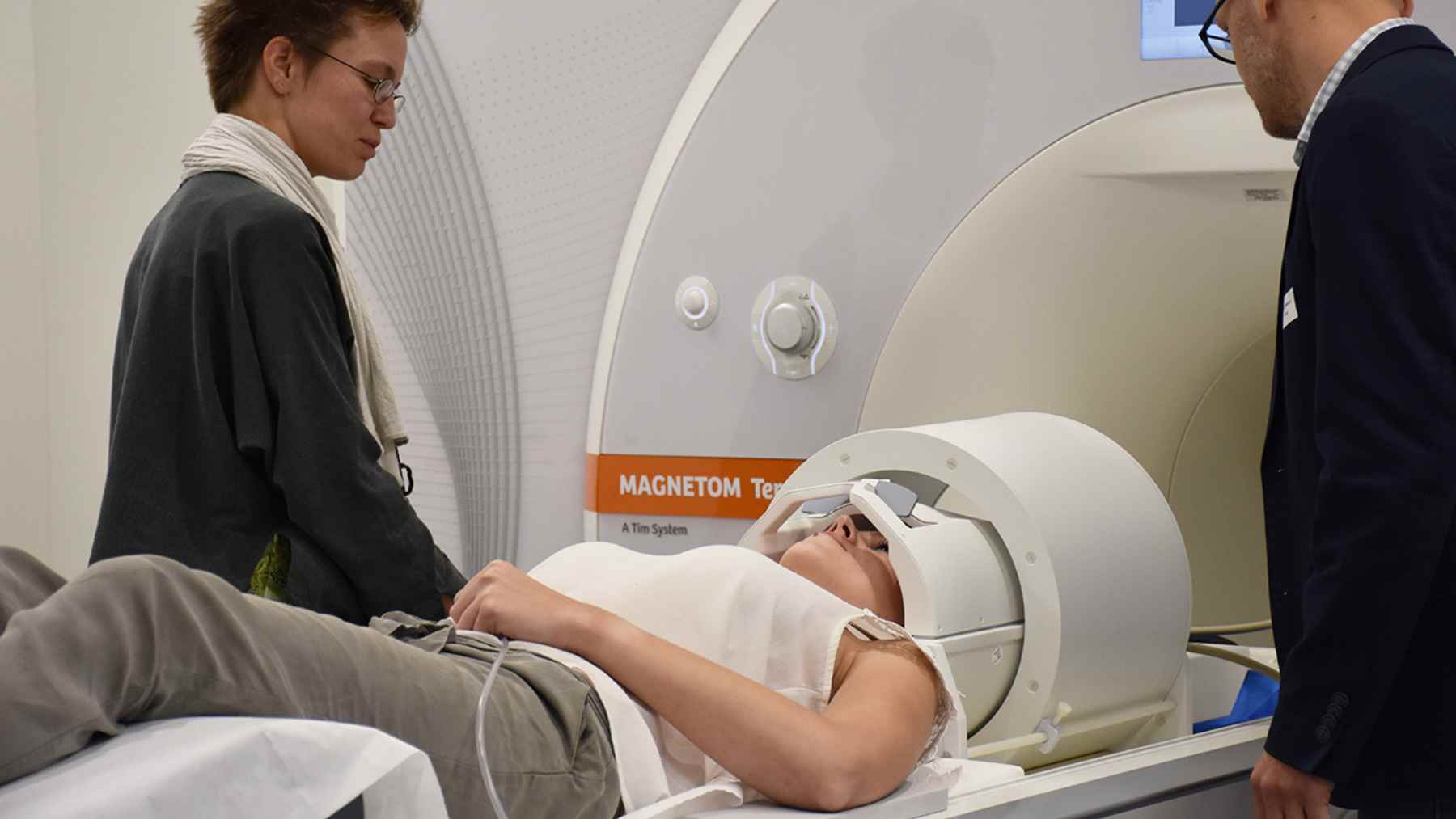 A volunteer lies on an MRI table with a head coil in place while researchers stand nearby, preparing a high-field brain scan experiment.