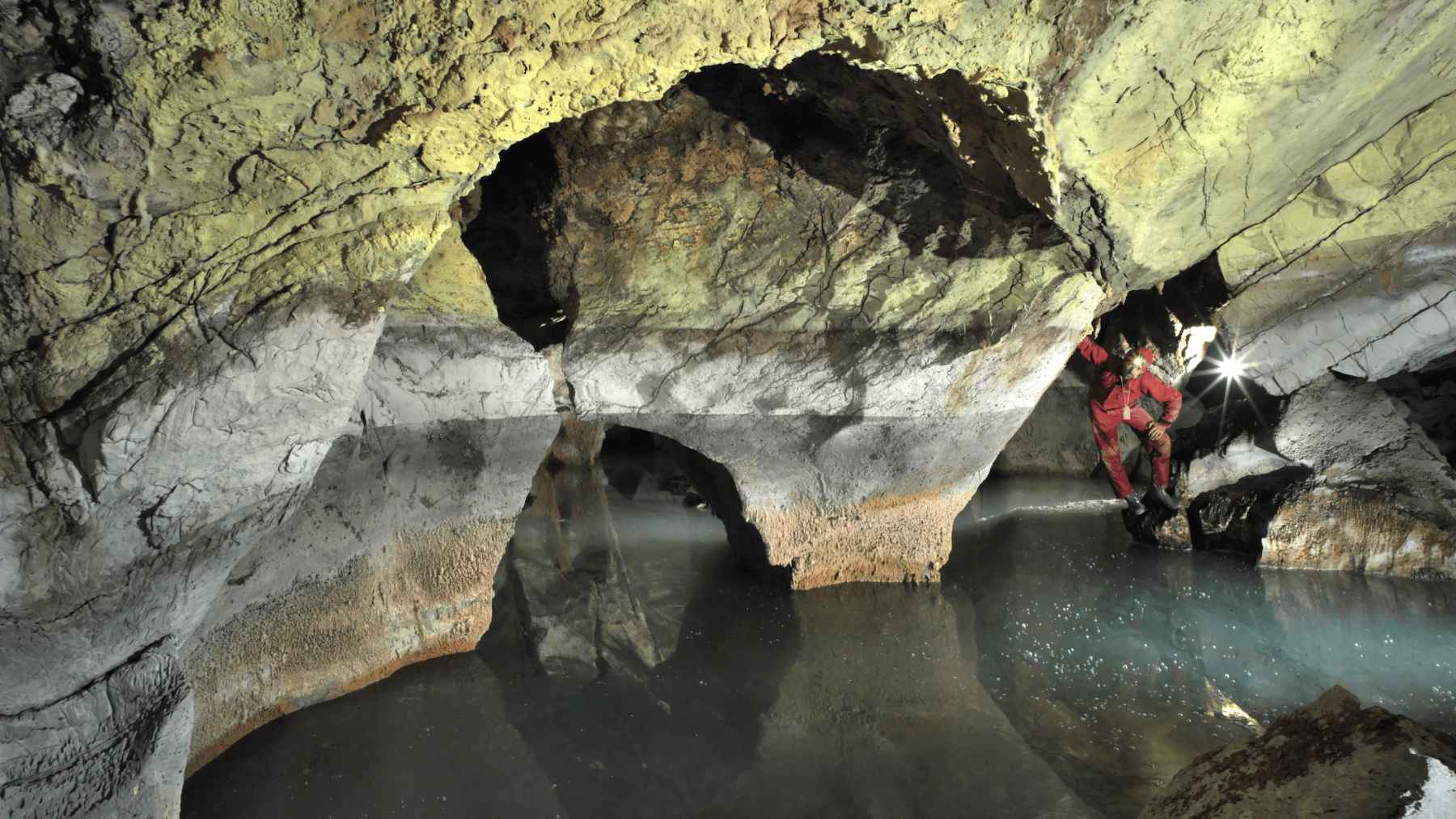 Caver standing beside Lake Neuron, a thermal underground lake inside Atmos Cave 127 meters below Albania