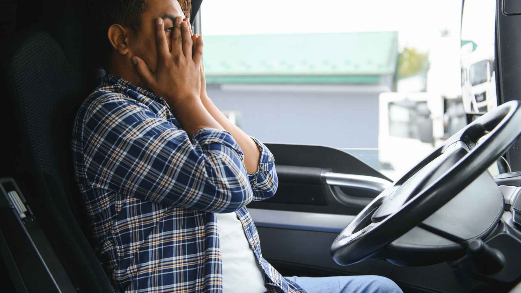 Truck driver sitting in a cab with hands on his face after receiving news about a license cancellation.