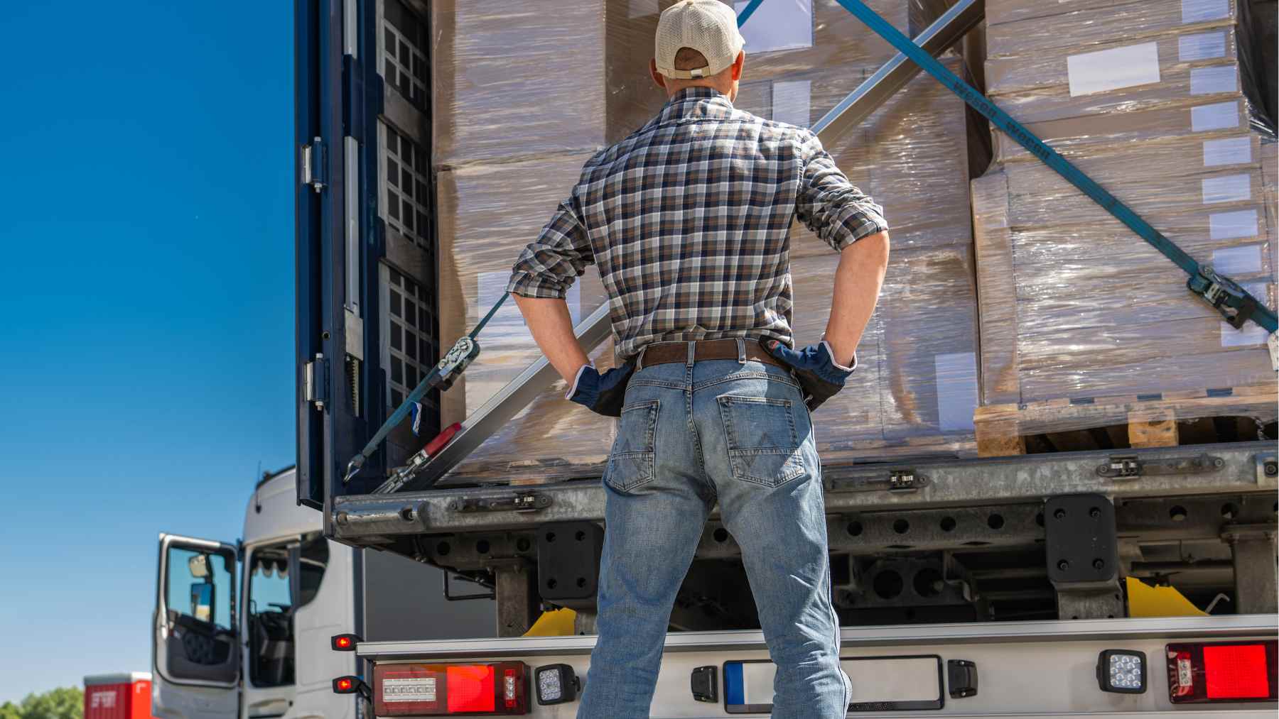 A truck driver stands at the back of a semi-trailer loaded with shrink-wrapped pallets, a common target in cargo theft cases.