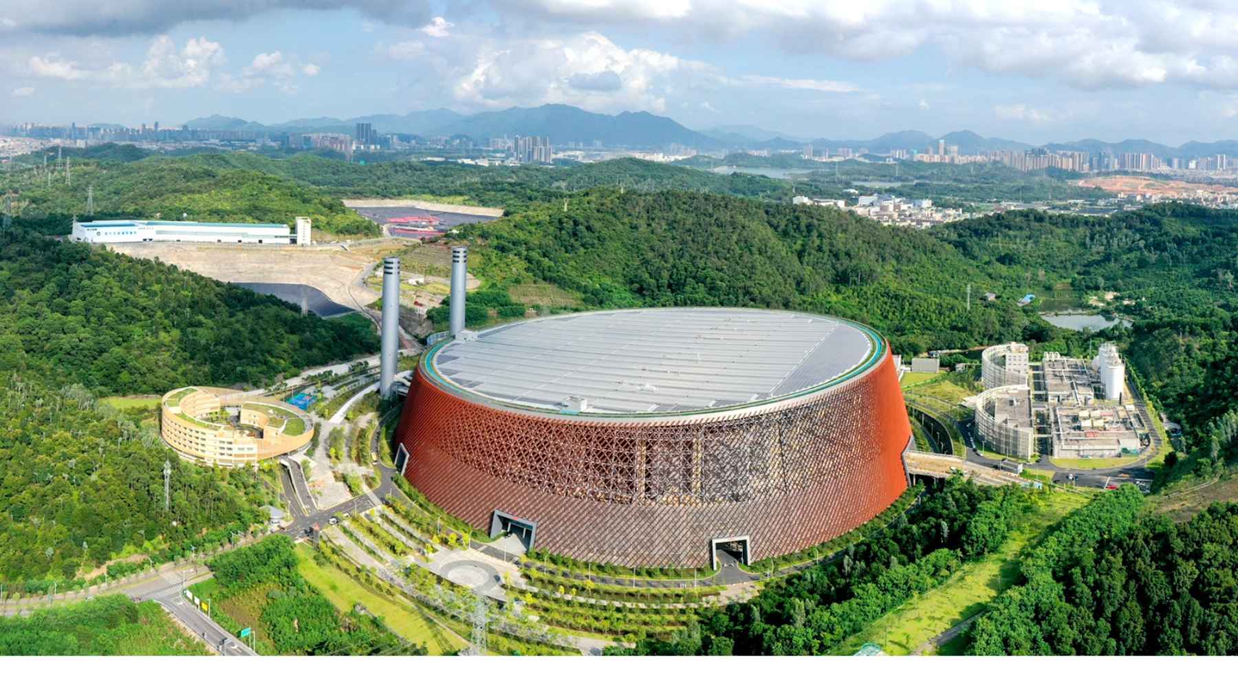 Aerial view of a large waste-to-energy incineration plant in China surrounded by green hills and nearby facilities.