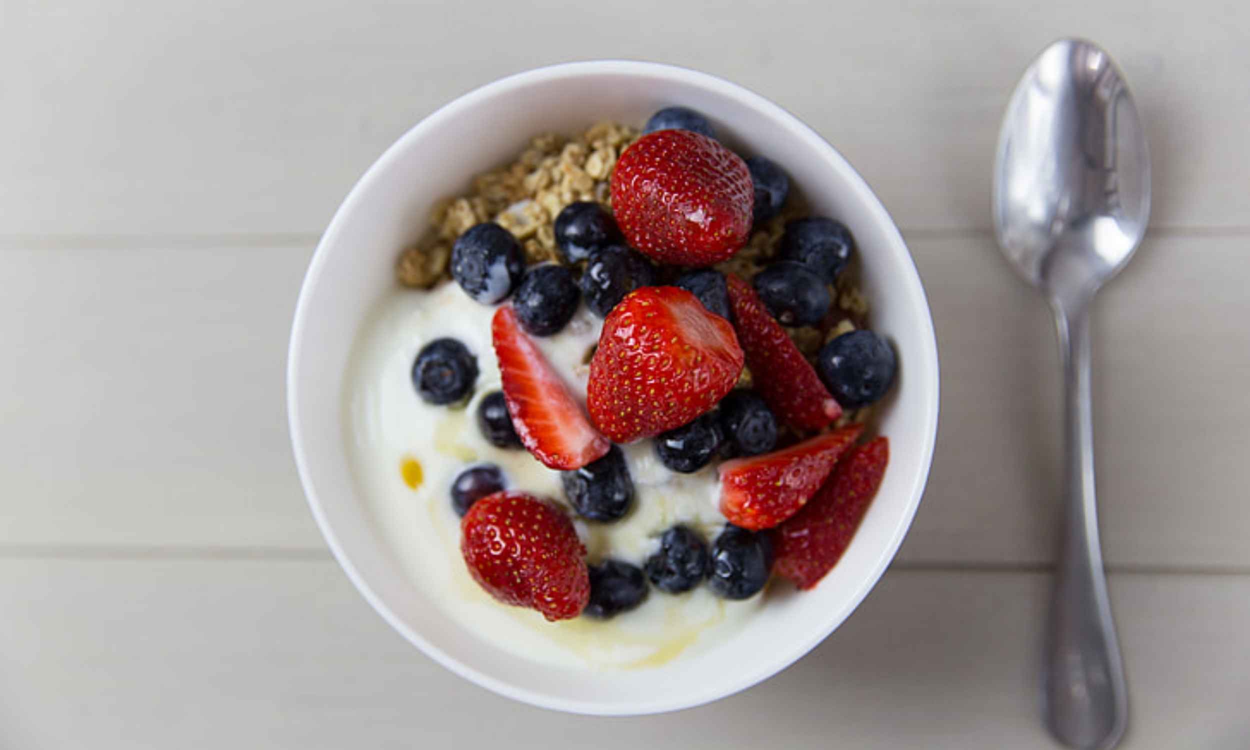 Bowl of plain yogurt topped with fruit and granola on a breakfast table