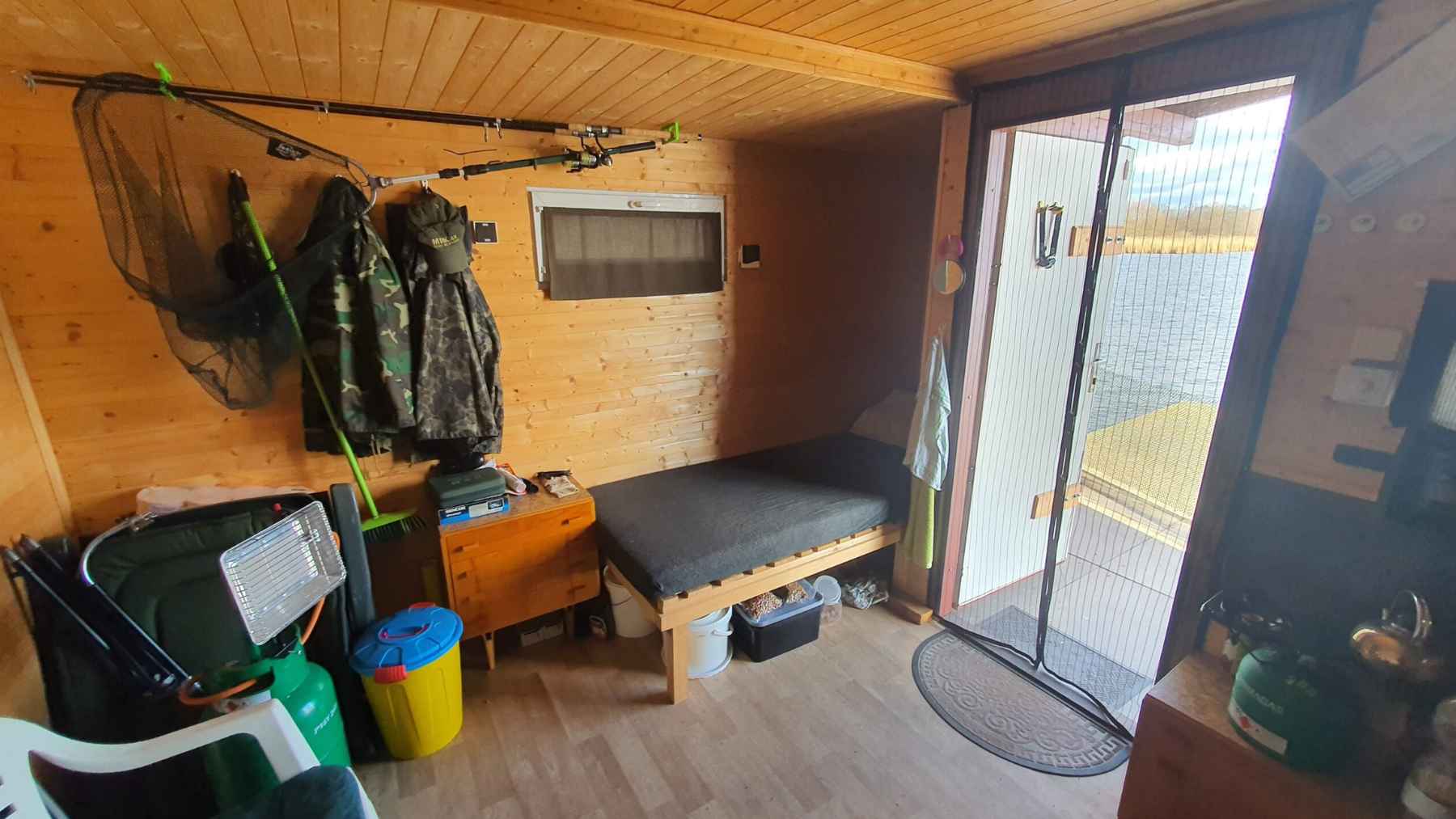Interior of a small wooden fishing hut at Hermanicky Pond near Ostrava, with a bench bed and door opening to the lake.