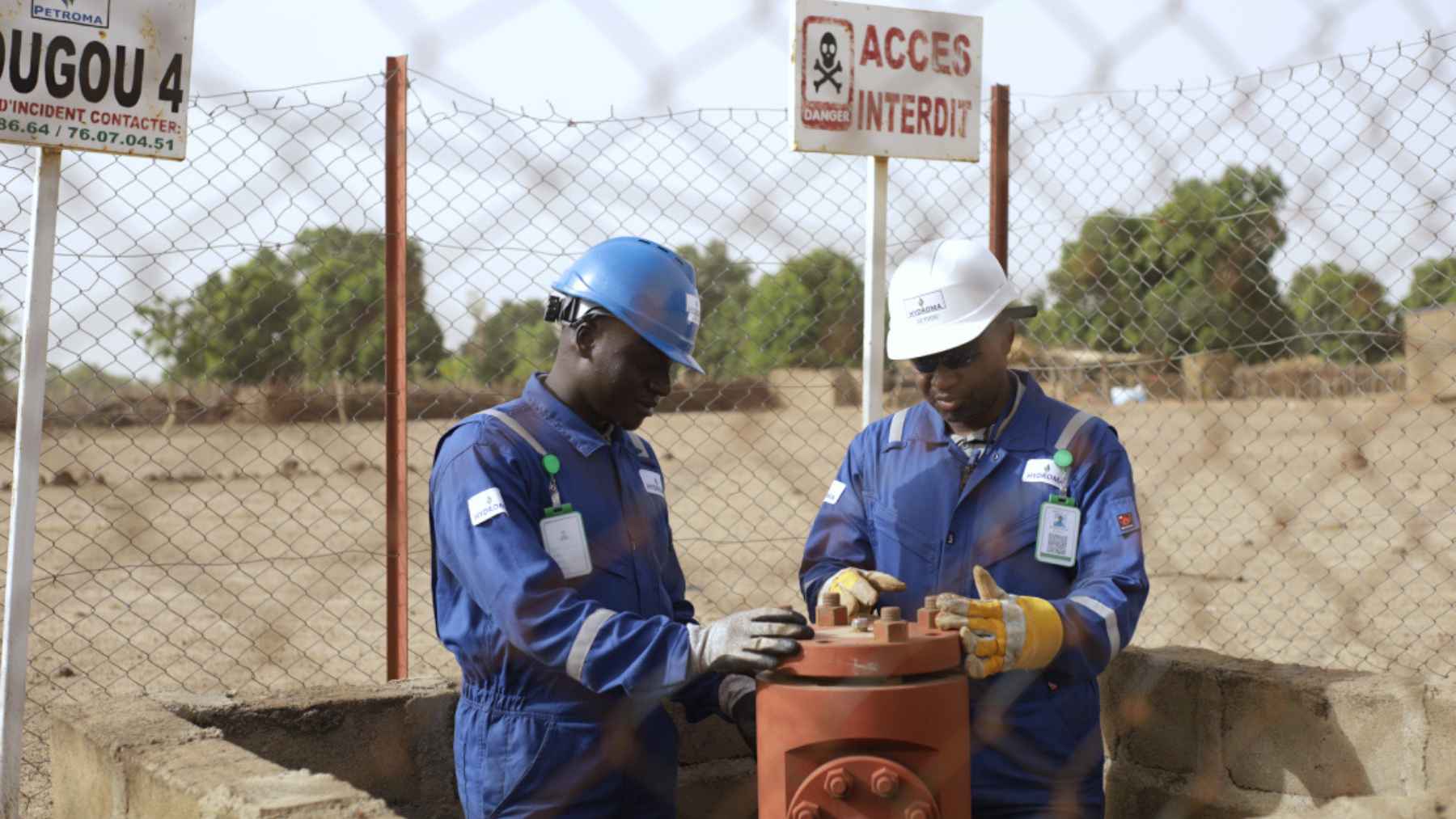 Two workers in hard hats inspect equipment at a drilling site, reflecting efforts to explore for natural hydrogen in the Earth’s crust.