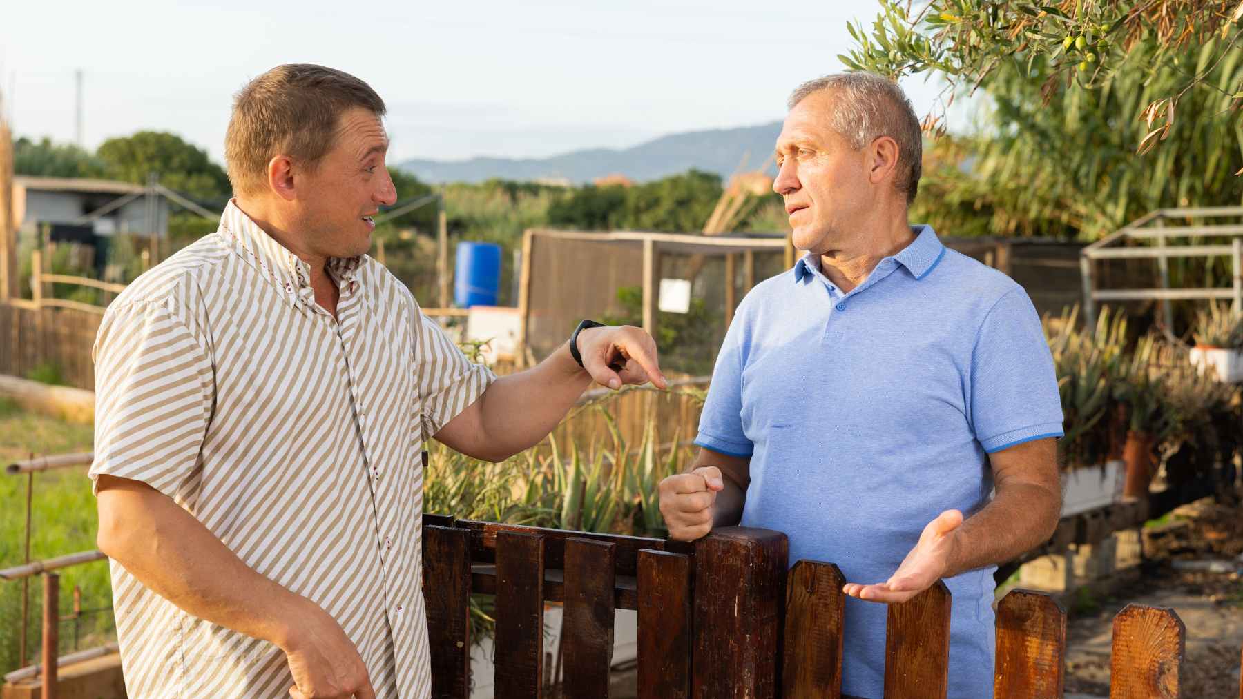 Two neighbors talk by a backyard fence near a garden, illustrating how a simple favor can trigger an unexpected property tax reassessment.