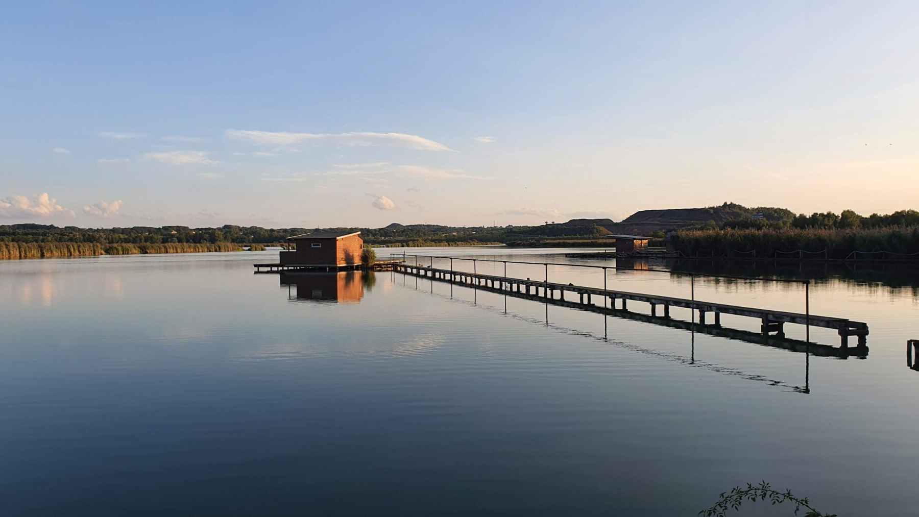 Fishing hut on stilts at Hermanicky Pond near Ostrava, linked by a narrow walkway over calm water at sunset.