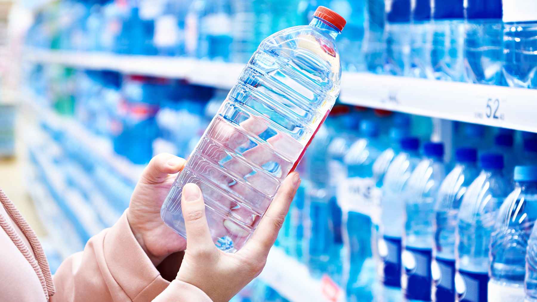 Hand holding a plastic water bottle in a store aisle, highlighting concerns about microplastics in bottled water.