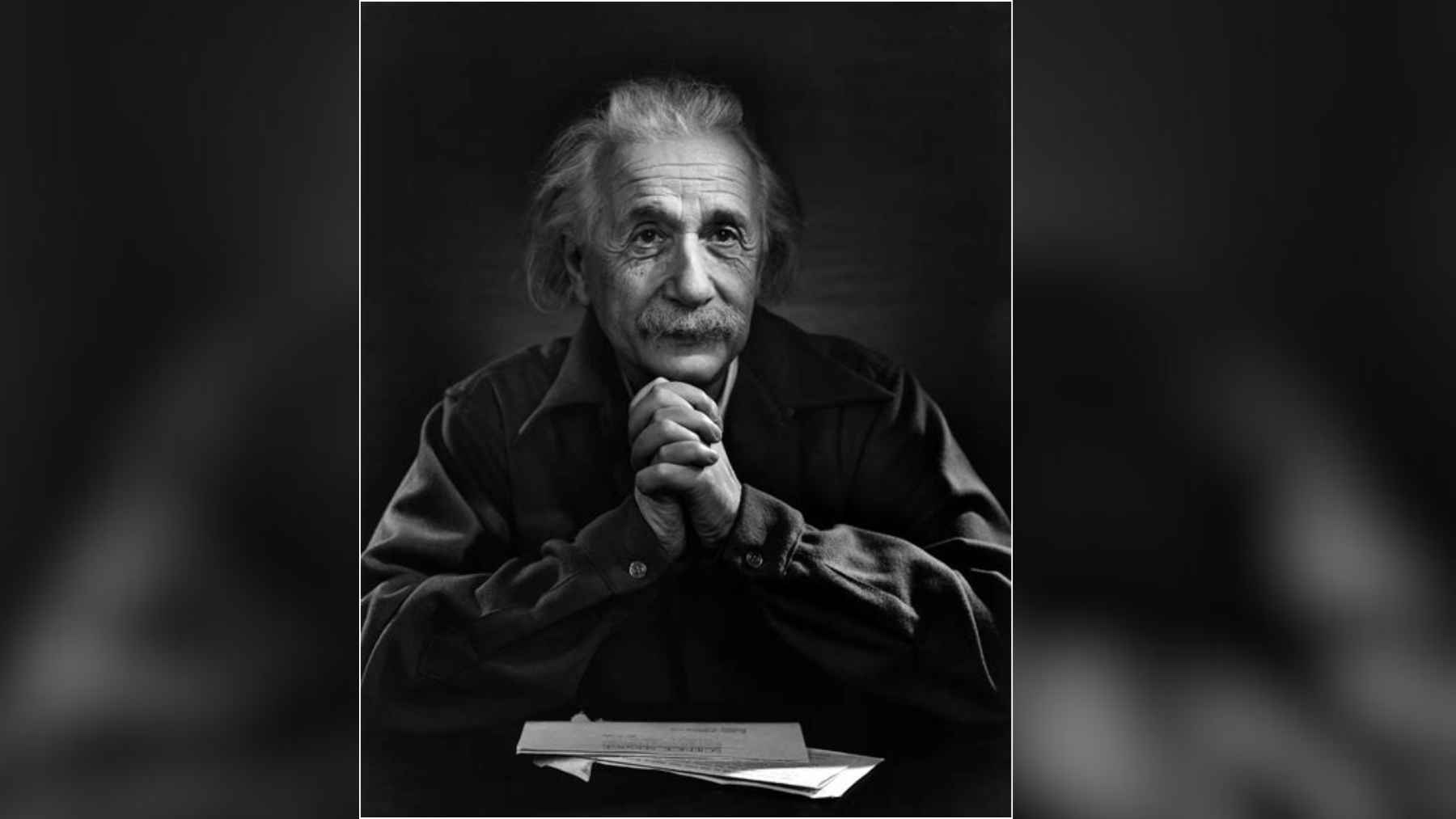1948 portrait of Albert Einstein by Yousuf Karsh, showing the physicist seated with his hands clasped beside papers on a table