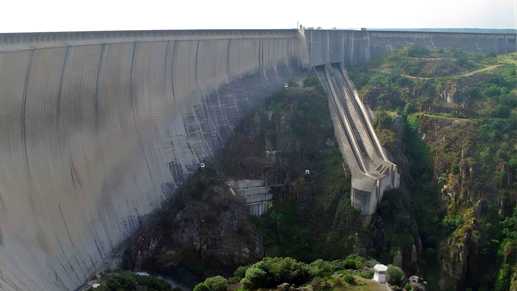 Side view of Almendra Dam in Spain showing its विशाल concrete wall, spillway structure, and rocky gorge below.