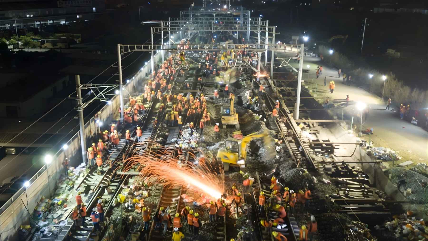 Hundreds of railway workers rebuilding tracks at night in China, illustrating a high-speed rail connection completed in a single operation.