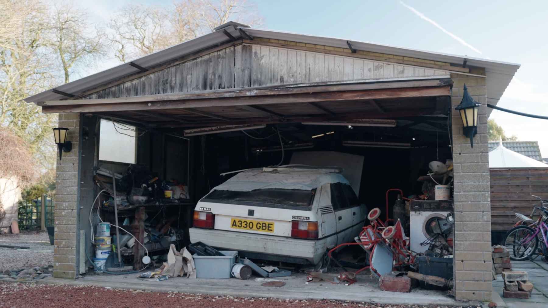 White Citroen BX parked inside a cluttered garage after decades in storage, surrounded by tools, boxes, and household items.