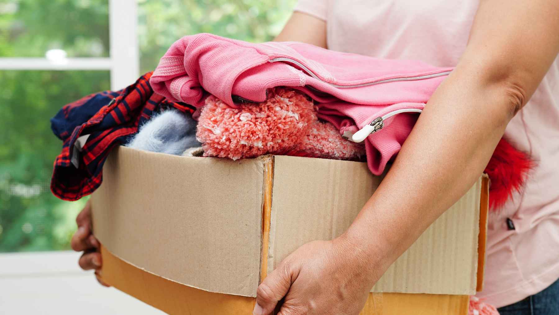Person holding a box of donated clothes during a closet cleanout at home