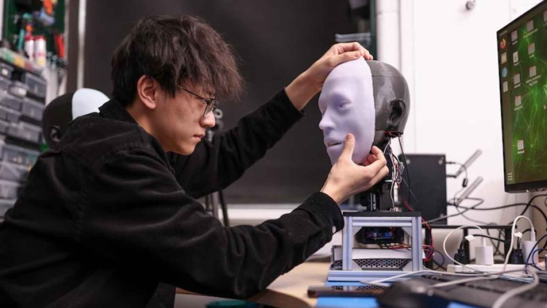 Researcher adjusting the silicone face of EMO humanoid robot designed to learn speech and lip movements through AI training.