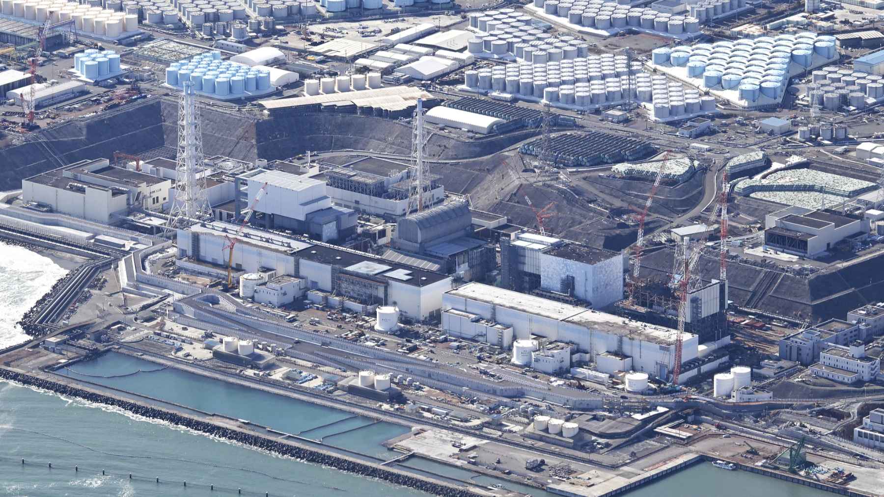 Dark image with an industrial facility visible at the top, illustrating the Fukushima nuclear site tied to research on microbial life in radioactive water.