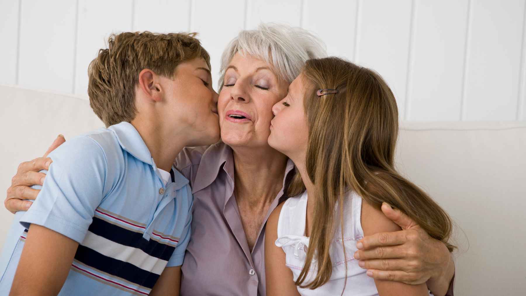 Grandmother receiving kisses from two grandchildren, illustrating a study on caregiving, memory, and brain health in older adults