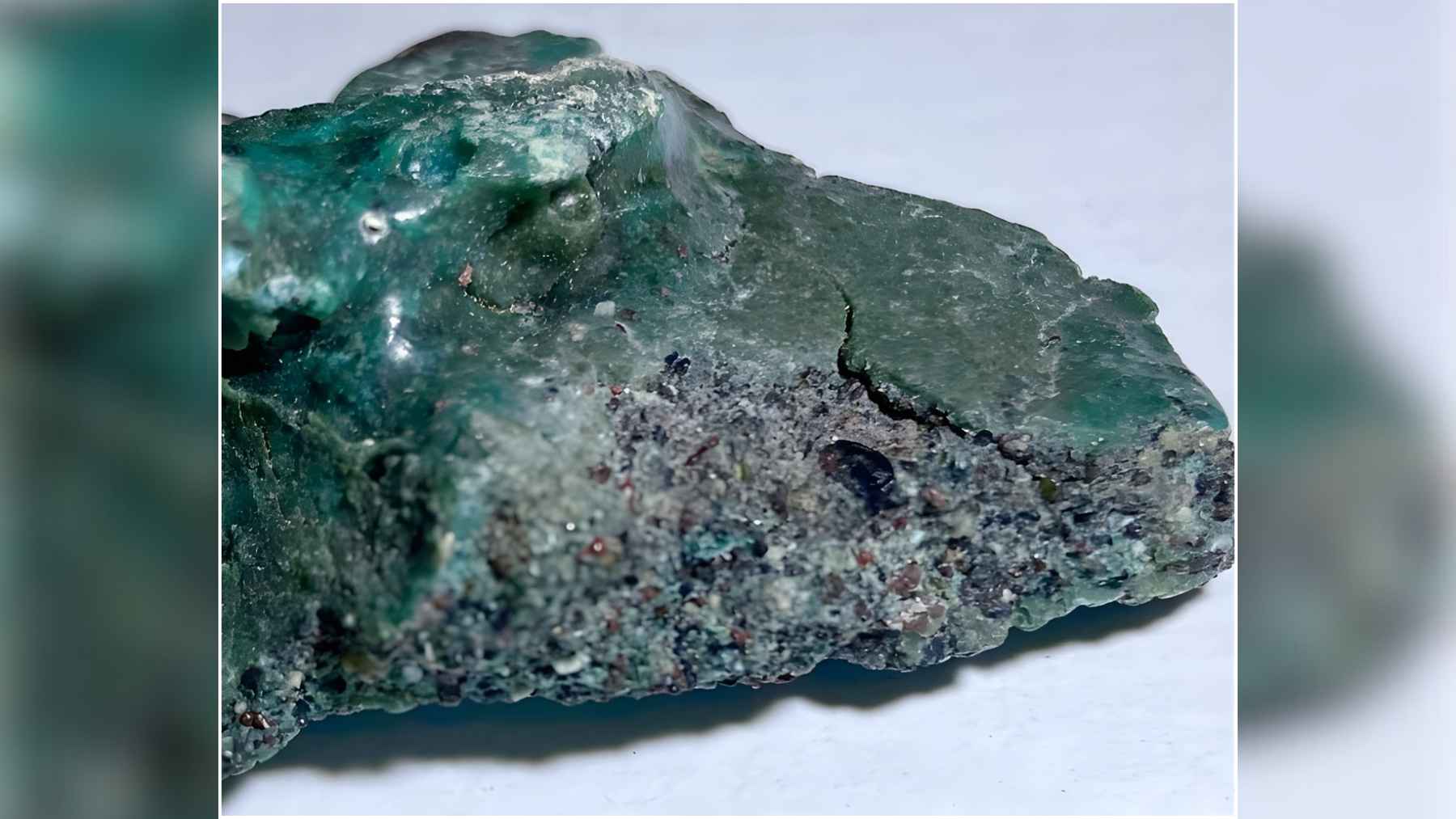 Close-up of a green plastic rock fragment showing fused plastic, sand, and small sediment particles.