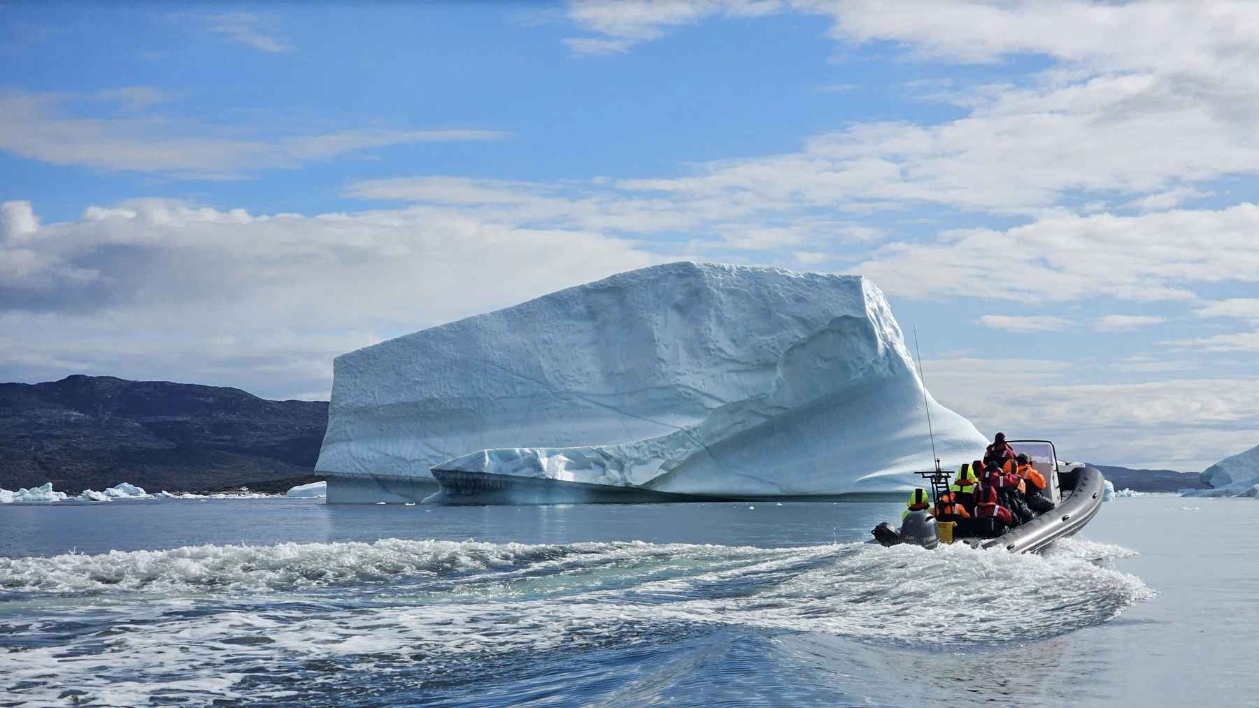 Small boat passing a massive iceberg off Greenland, illustrating the coastal environment affected by ice loss, land uplift, and local sea-level change