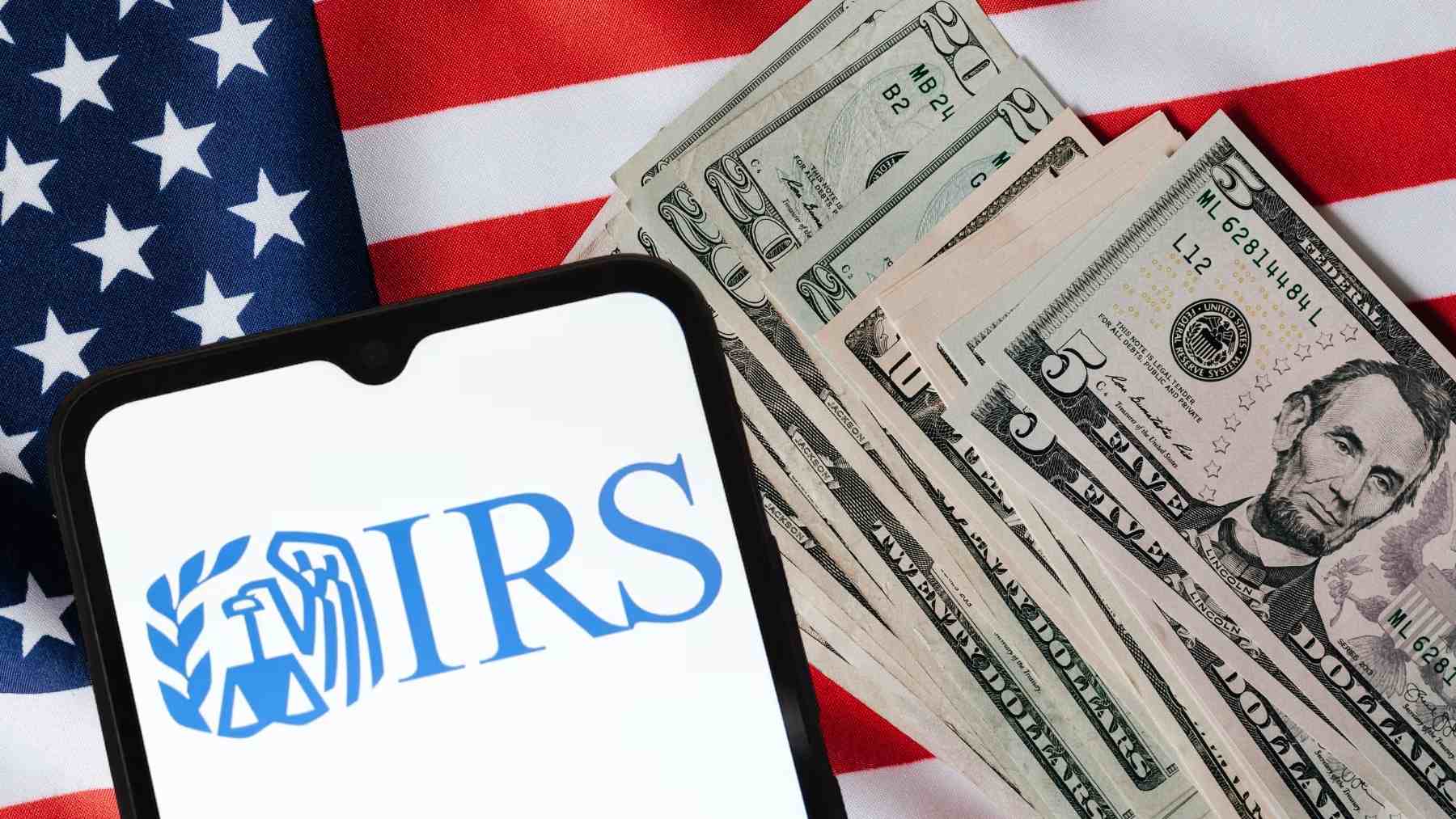 IRS logo on a smartphone next to U.S. dollar bills and an American flag