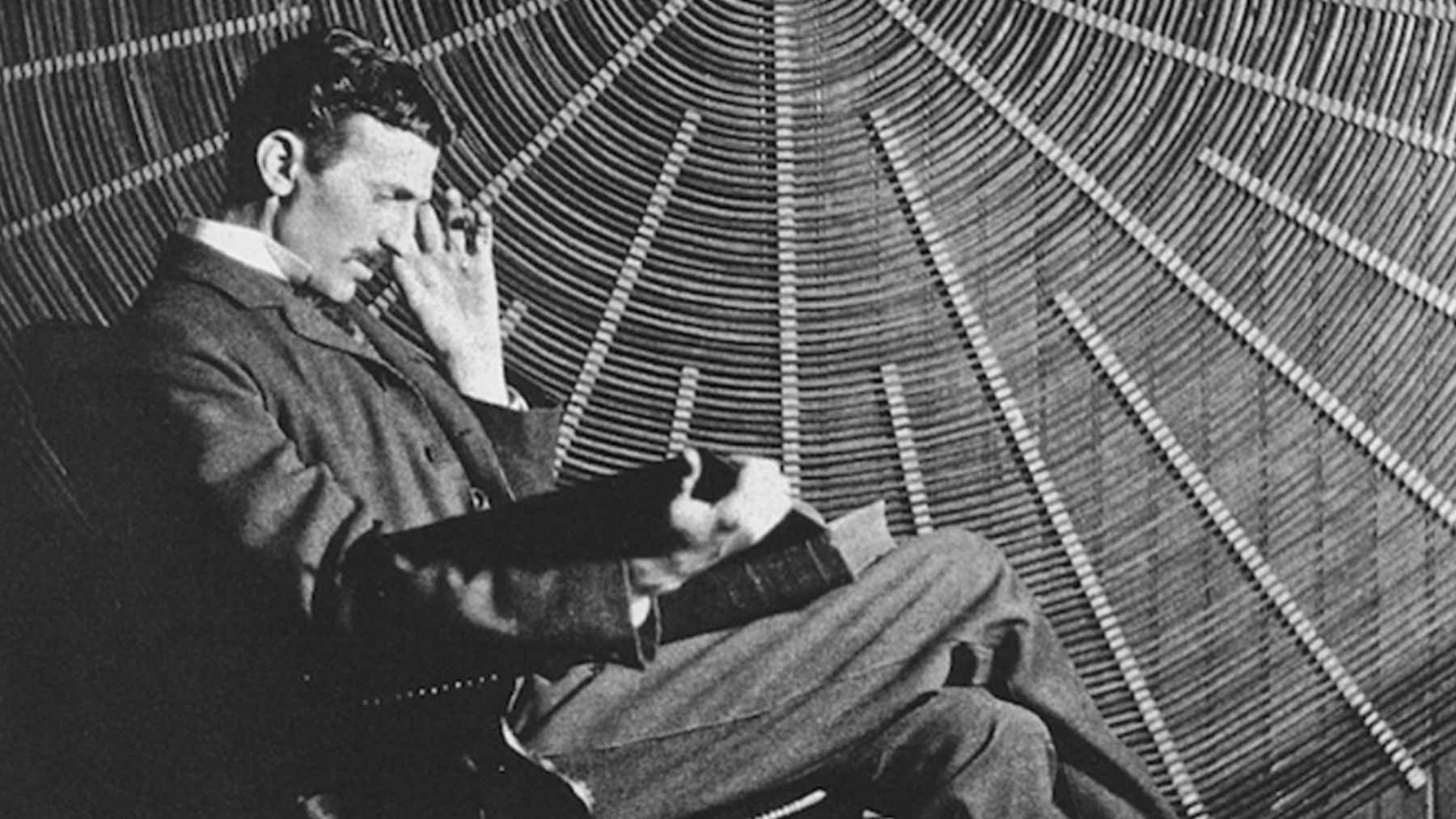 Portrait of Nikola Tesla seated in a chair before a circular laboratory backdrop