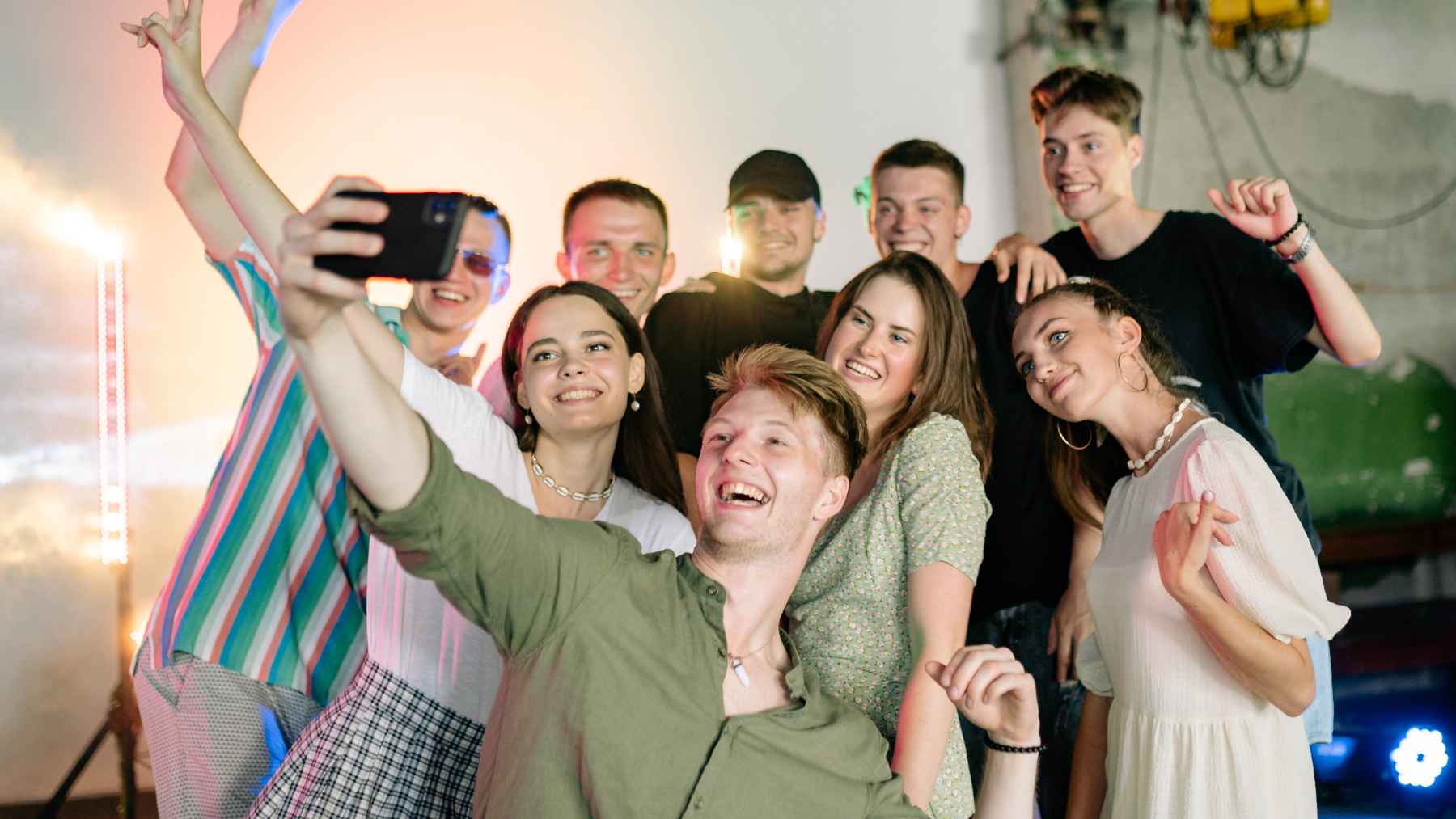 Group of young adults taking a selfie at a party, illustrating the contrast between social connection, friendship, and loneliness