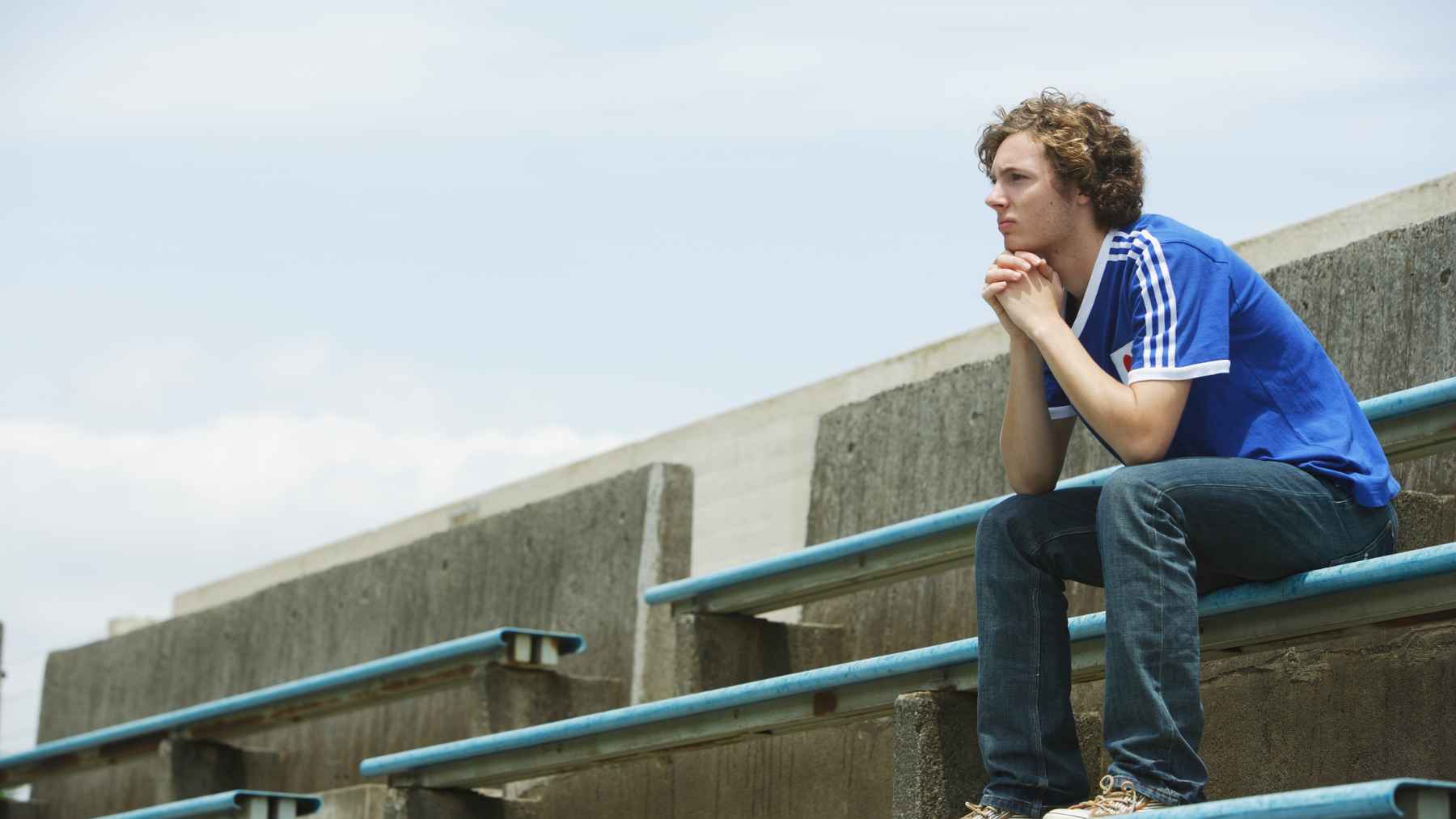 Young man sitting alone on empty bleachers, illustrating solitude, loneliness, and the psychological difference between being alone and feeling disconnected