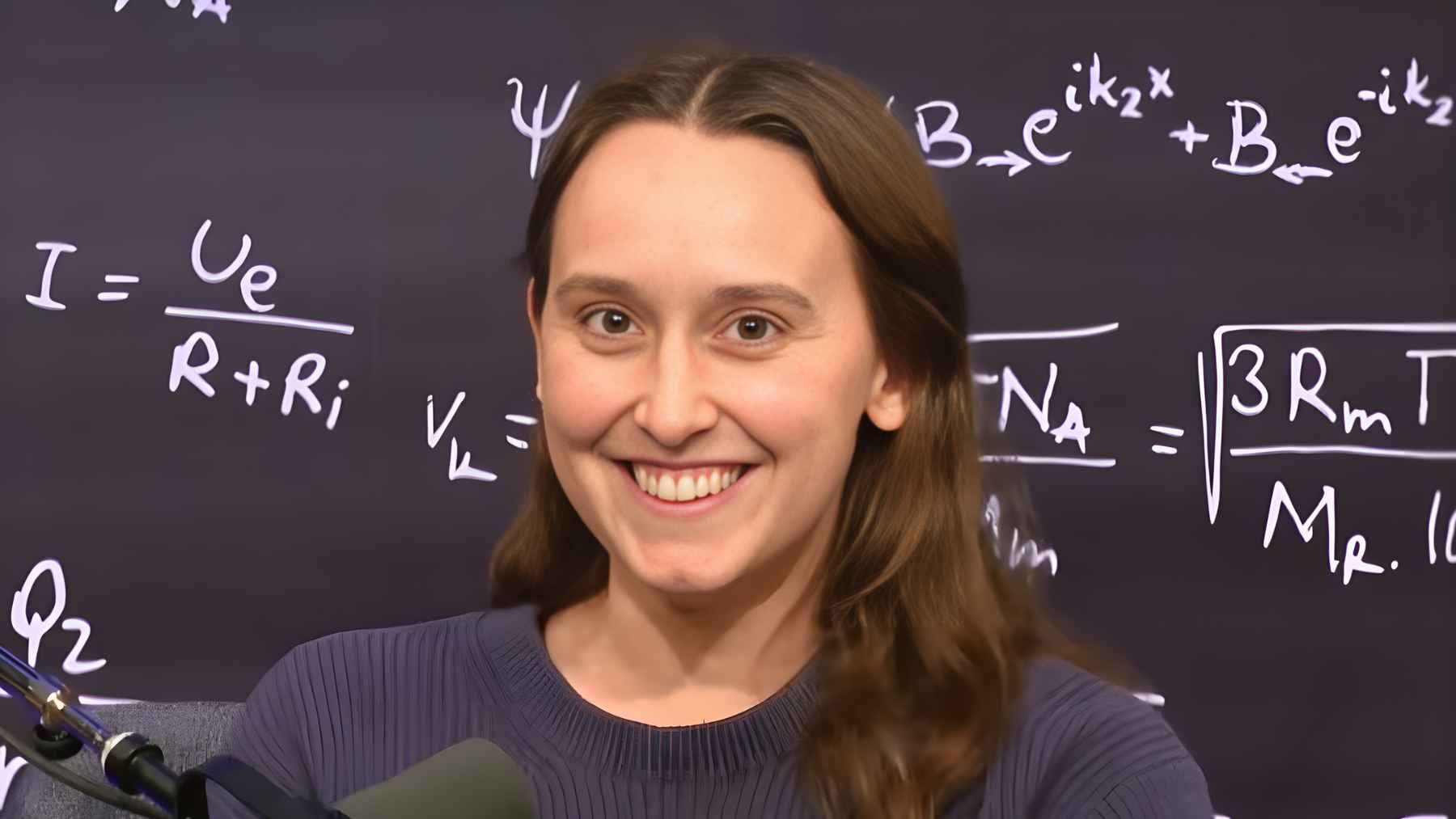 Physicist Sabrina Gonzalez Pasterski speaking in front of a blackboard filled with equations, illustrating her work in theoretical physics.