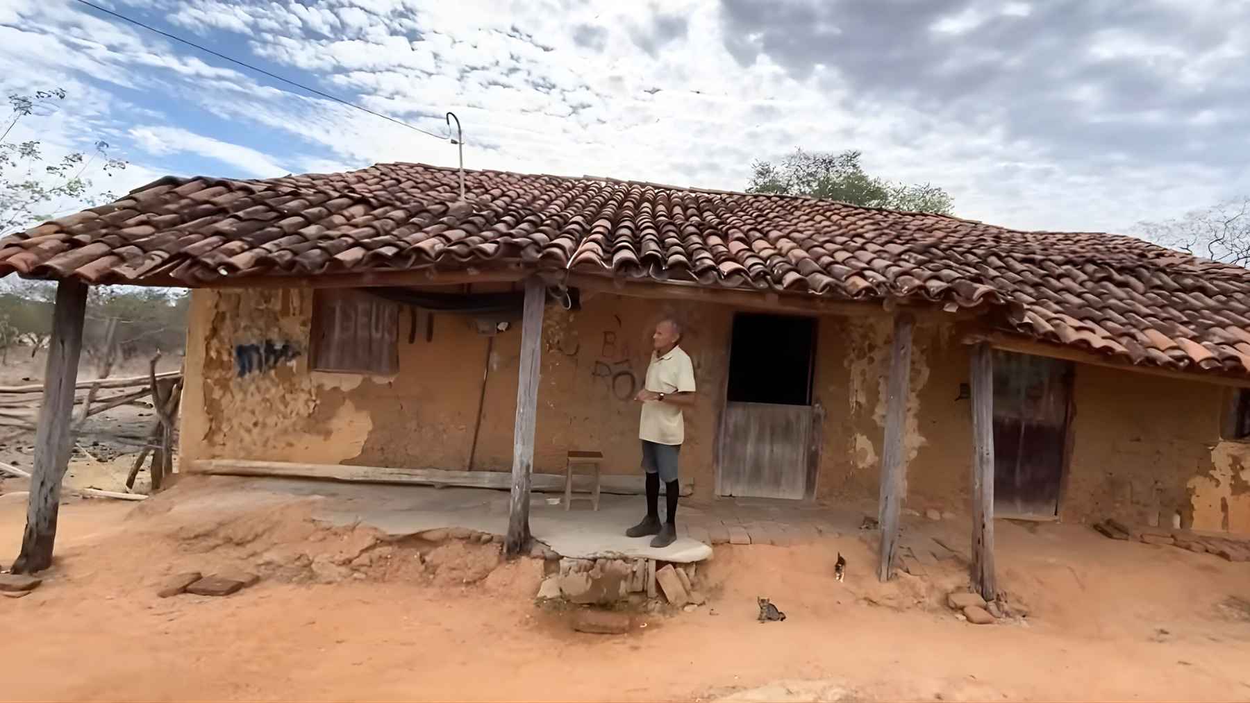 Elderly man standing outside his century-old adobe house in rural Brazil, illustrating a traditional life shaped by well water, firewood, and self-reliance