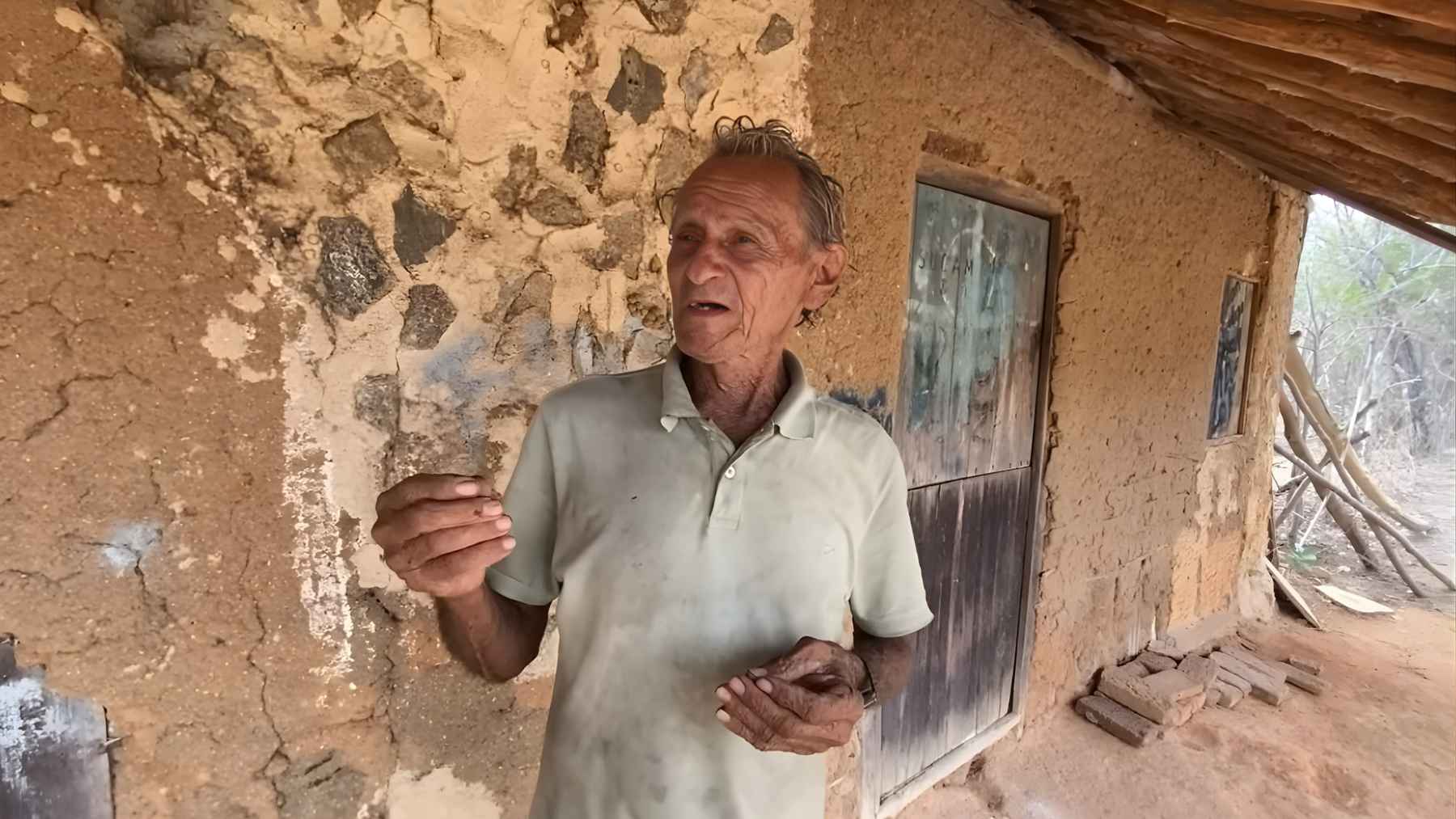 Seu Chiquinho standing beside the wall of his adobe house in rural Brazil, reflecting a life built around traditional materials and simple routines