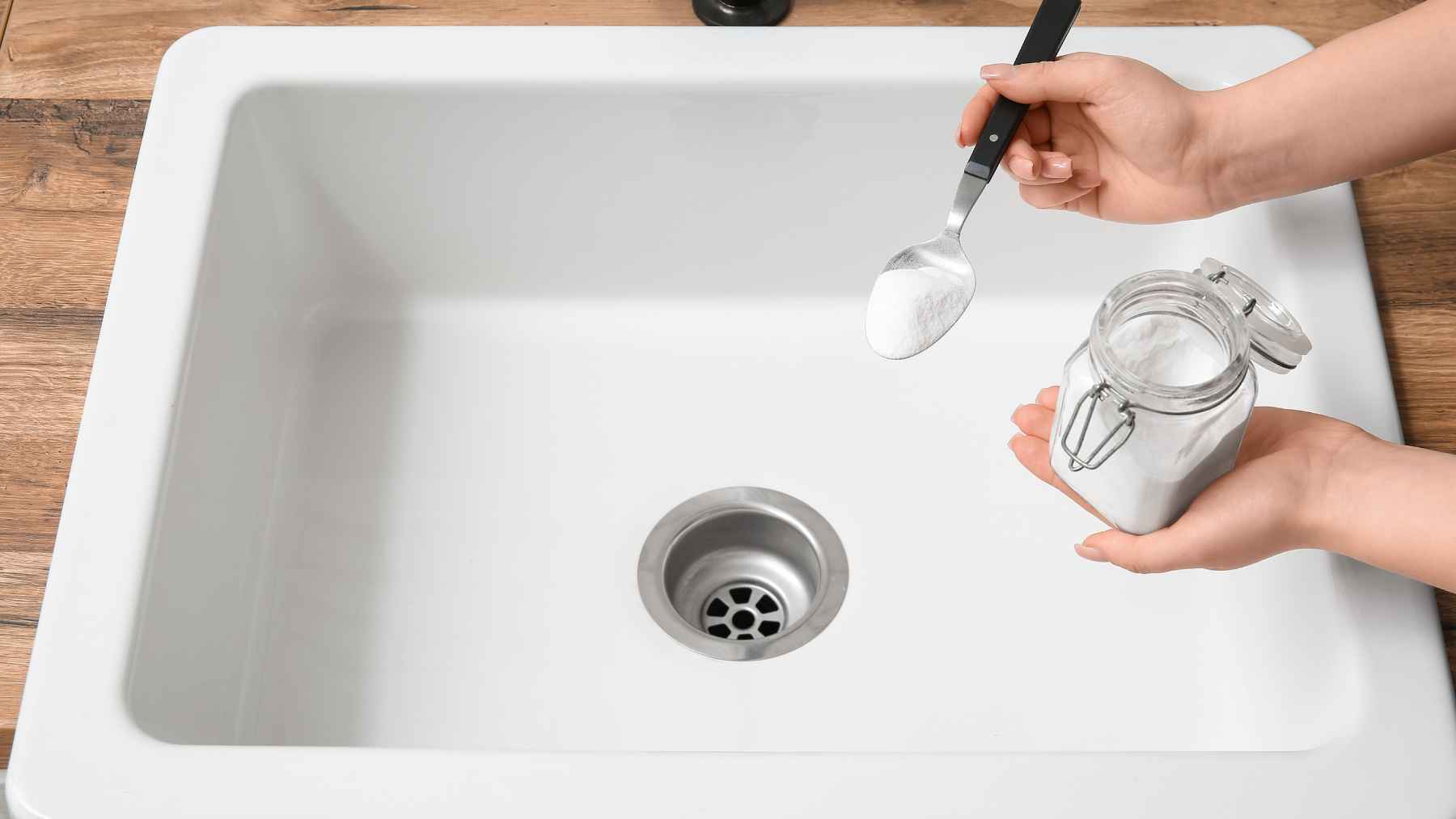 Person holding a spoonful of baking soda over a kitchen sink, a common household ingredient used in homemade insect control