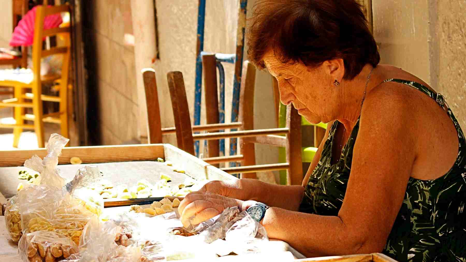 Older woman preparing homemade food at a table, reflecting the unseen work behind long-running family traditions.