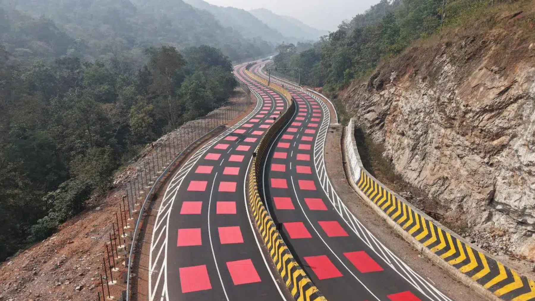 Curving highway in India with repeated red surface markings designed to slow traffic through a wildlife corridor in a mountainous area.