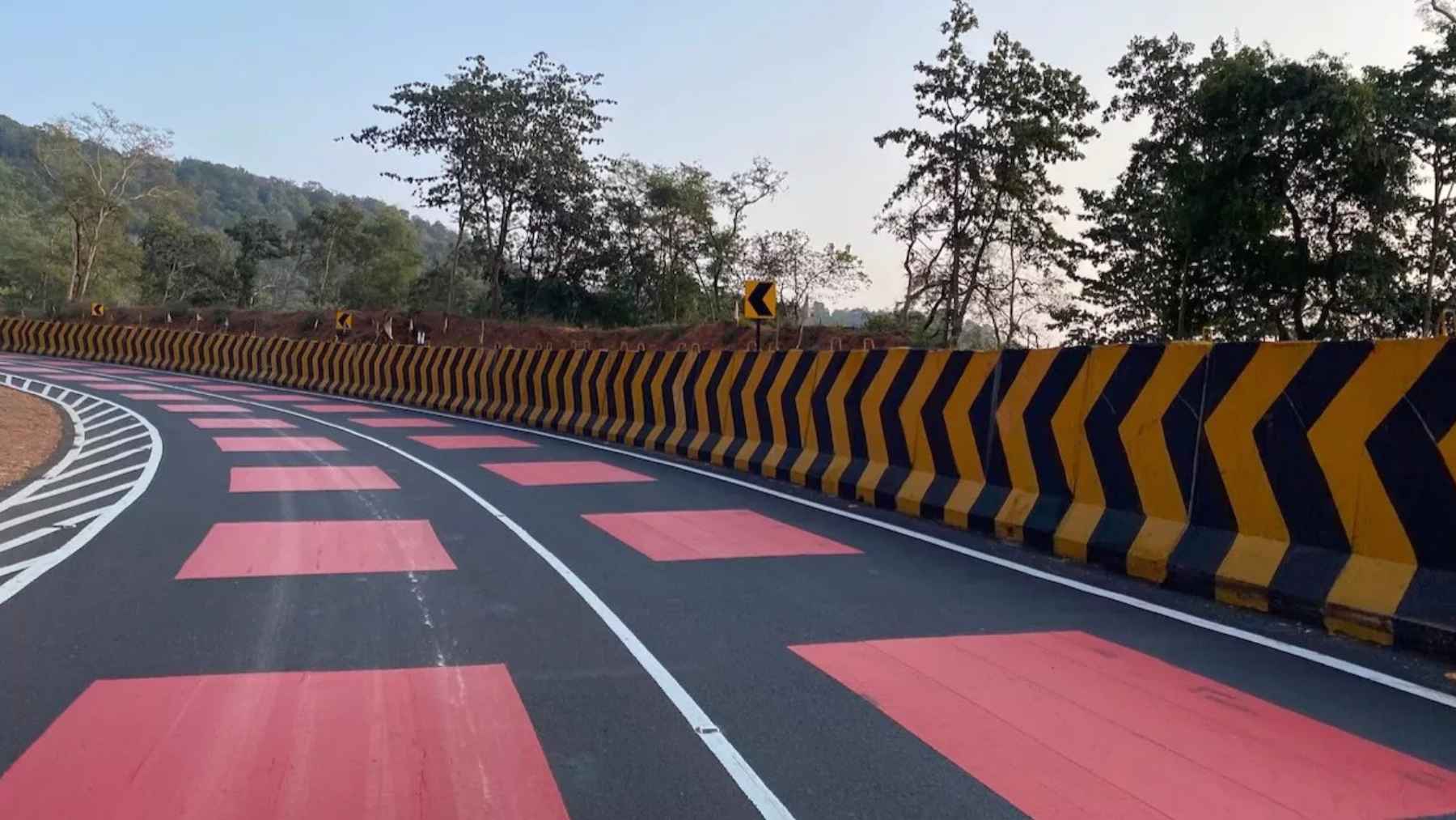 Red highway section in India with bright thermoplastic surface designed to slow drivers in a wildlife corridor with fencing and underpasses.
