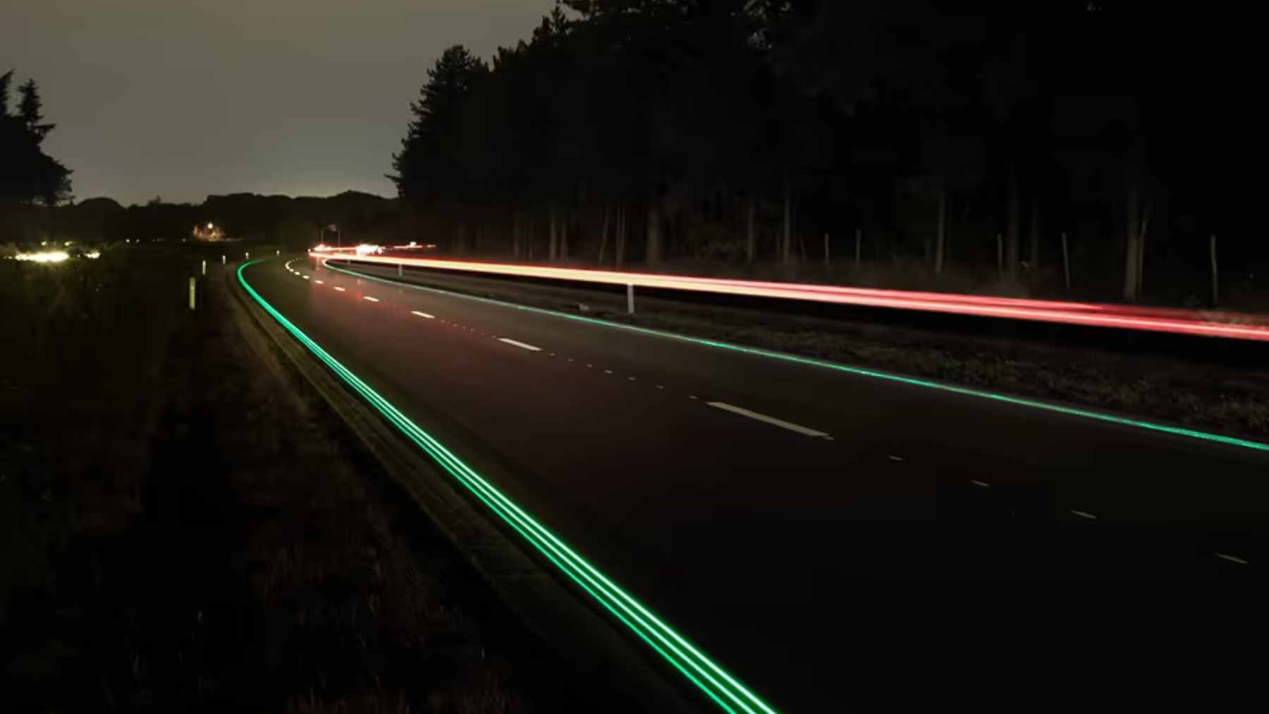 A dark roadway at night illuminated only by bright, glowing photoluminescent lane lines.