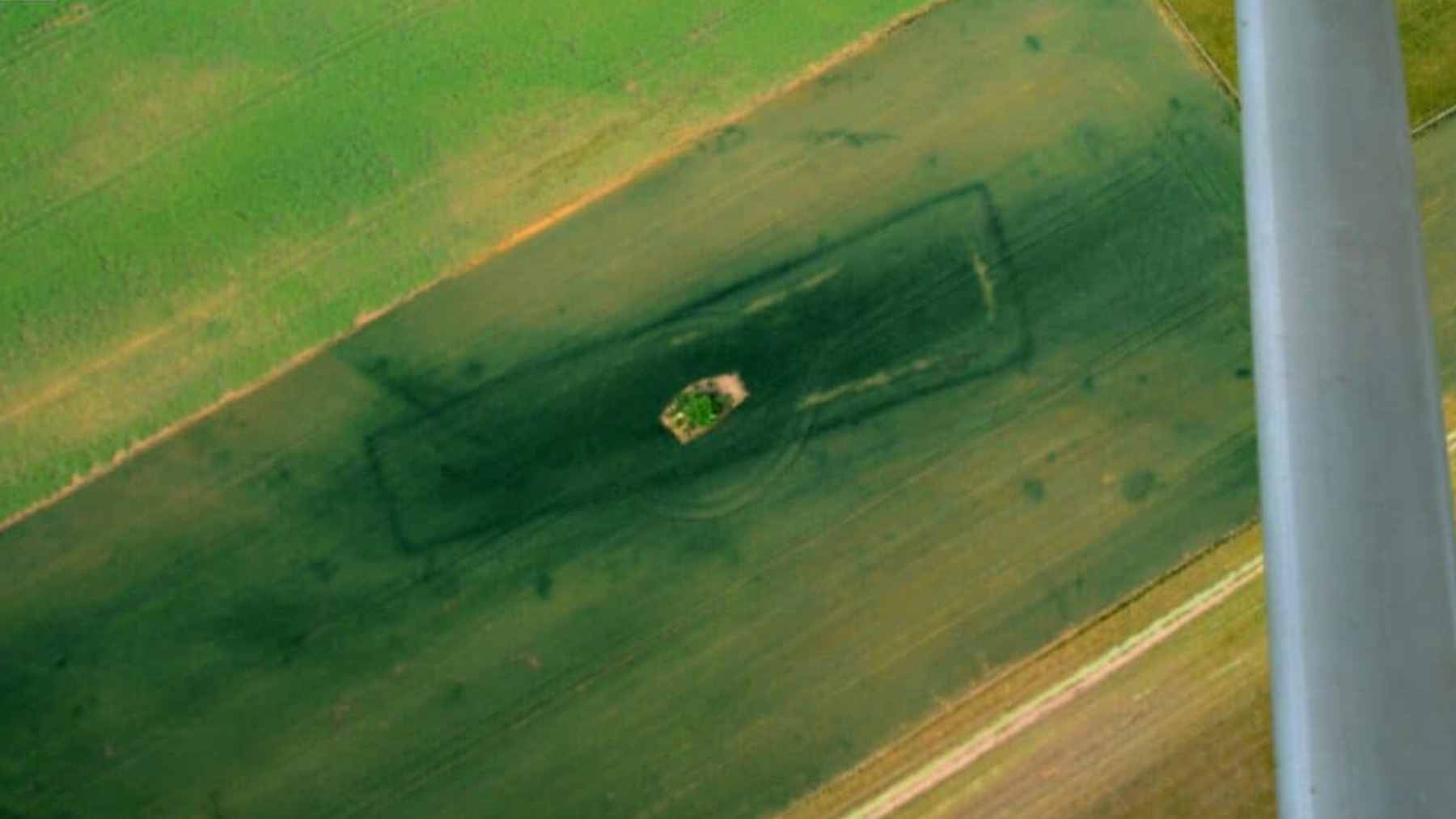 An aerial view of a harvested farm field in Bohemia with overlaid digital infrared highlights showing the outlines of prehistoric long barrows.
